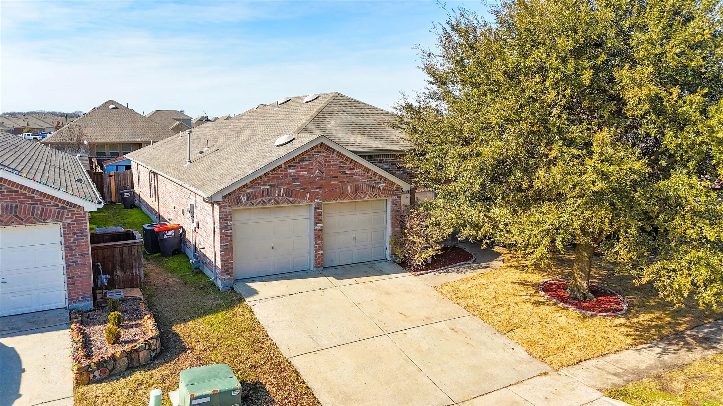 Brick-front residence featuring a two-car garage, concrete driveway, and a mature shade tree