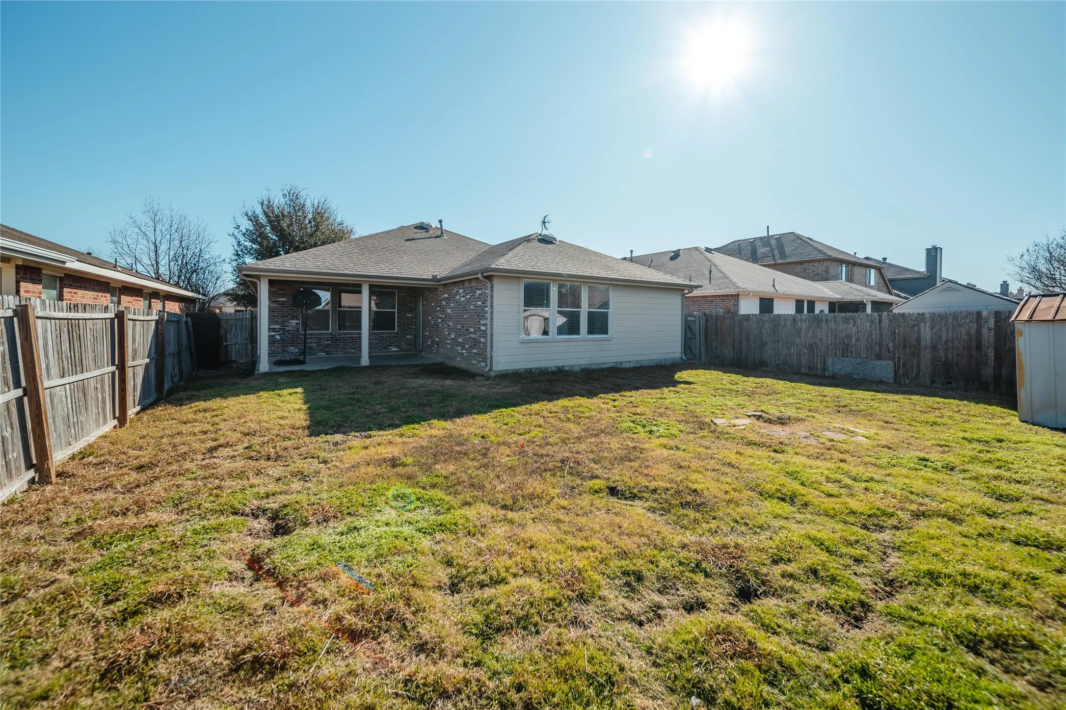 Expansive backyard featuring a covered patio with columns, wood fencing, and a detached storage shed