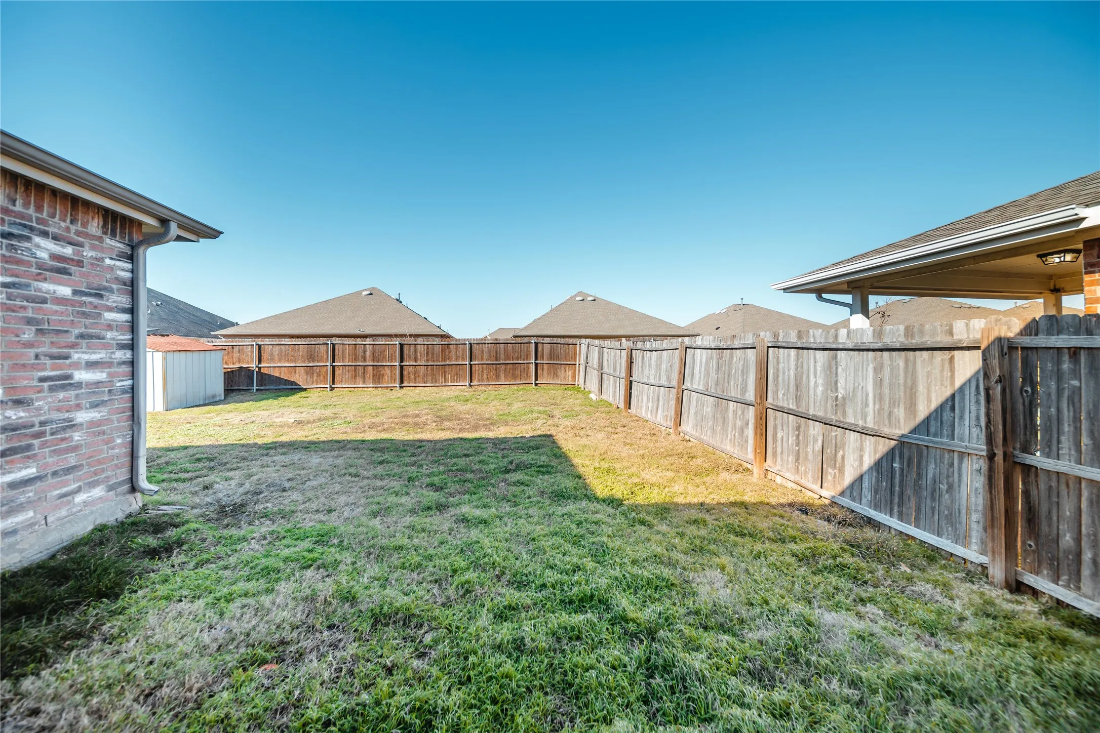 Expansive backyard featuring a wood privacy fence, a detached storage shed, and a brick exterior with white gutters