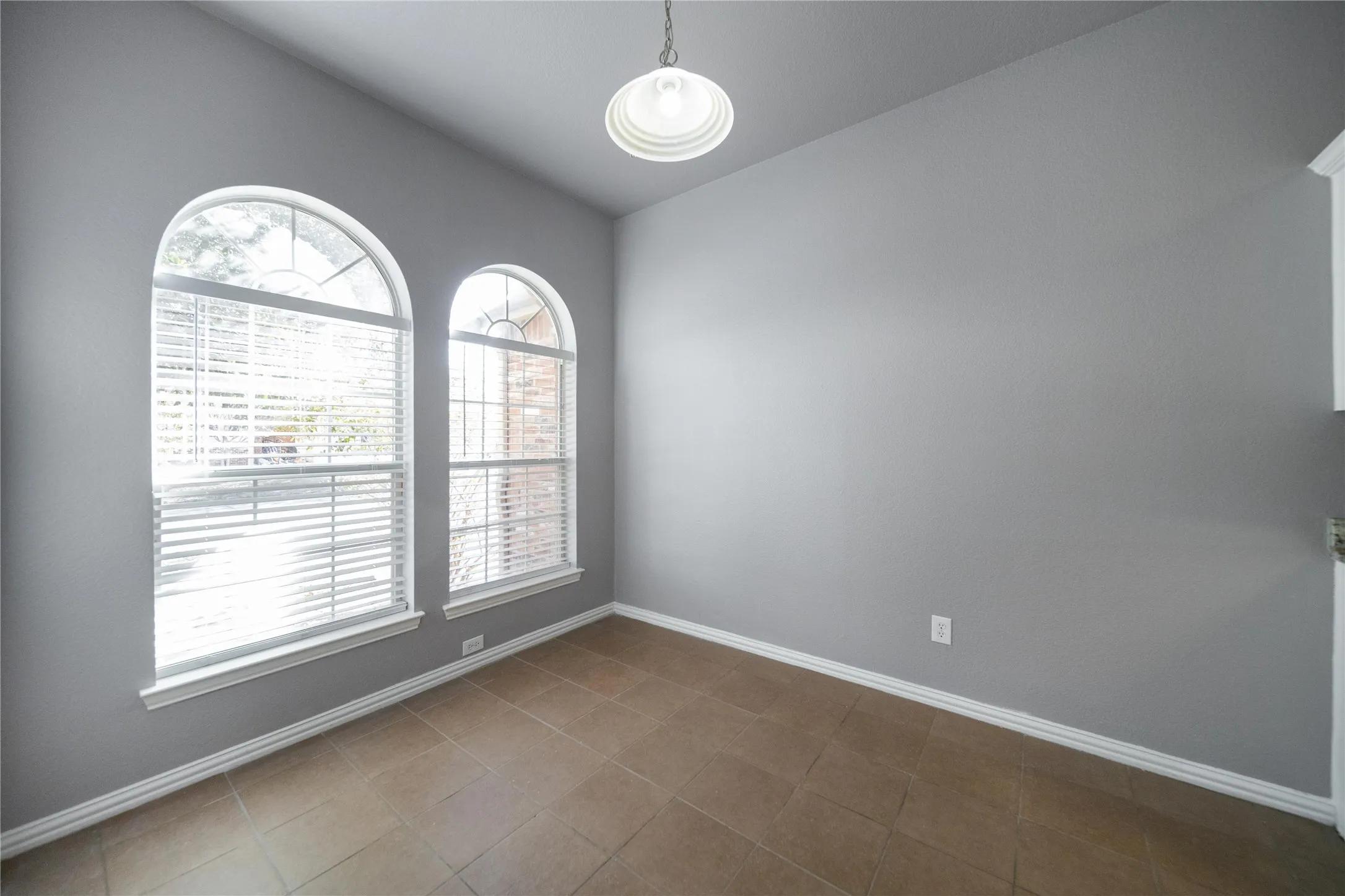 Room featuring two arched windows with internal blinds, tile flooring, and a ceiling-mounted light fixture