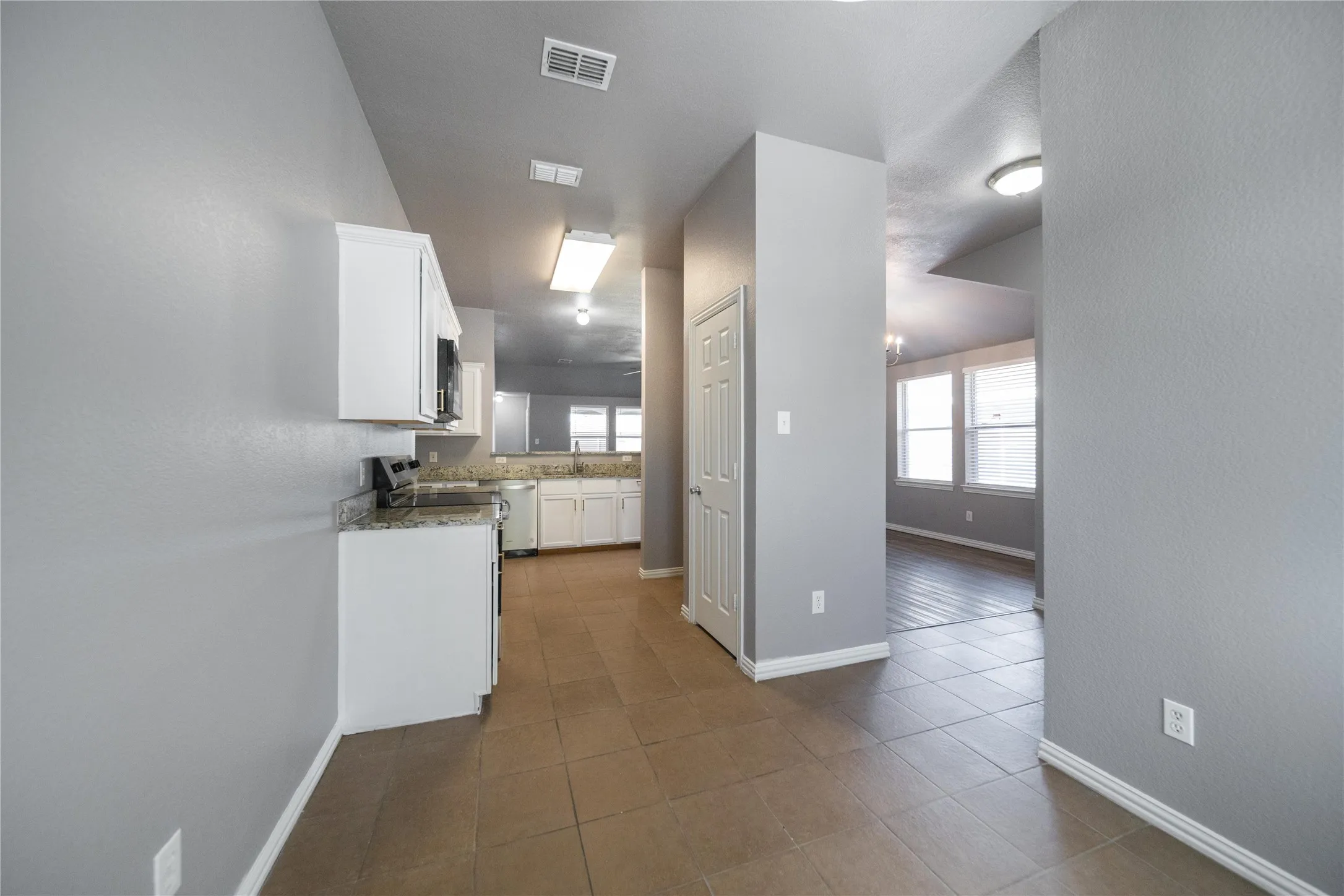 Kitchen featuring white cabinetry, light-toned granite-style countertops, stainless steel appliances, and tile flooring