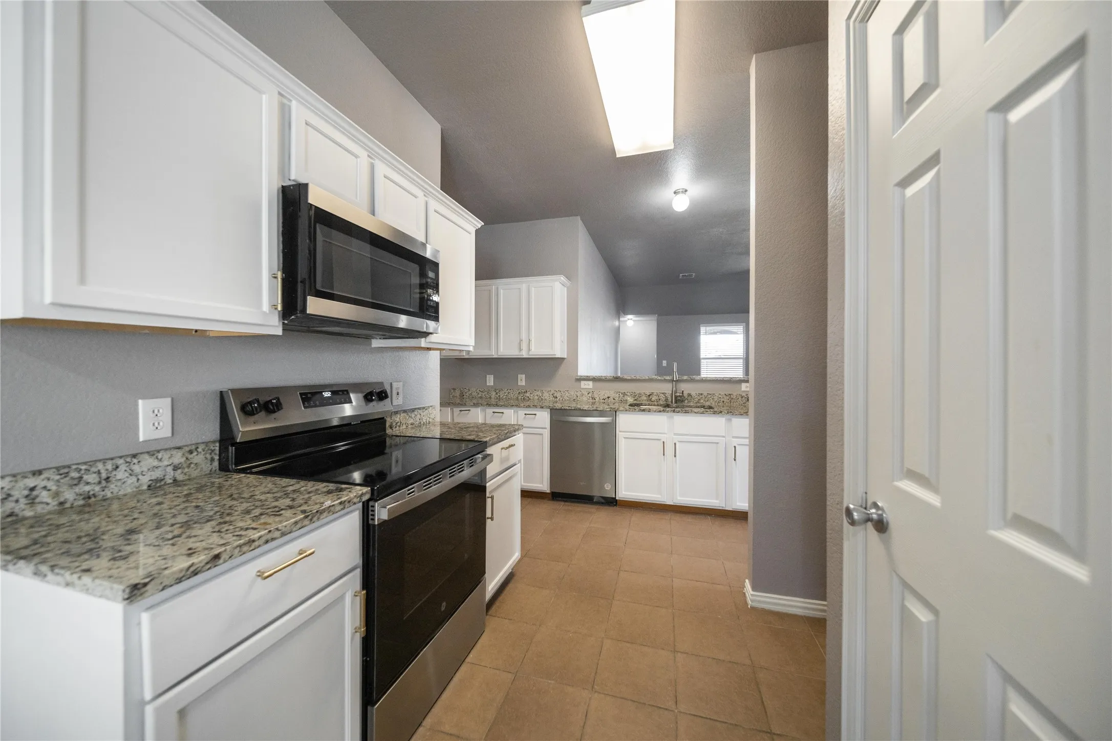 White cabinetry with gold-tone hardware, stainless steel appliances, and granite countertops