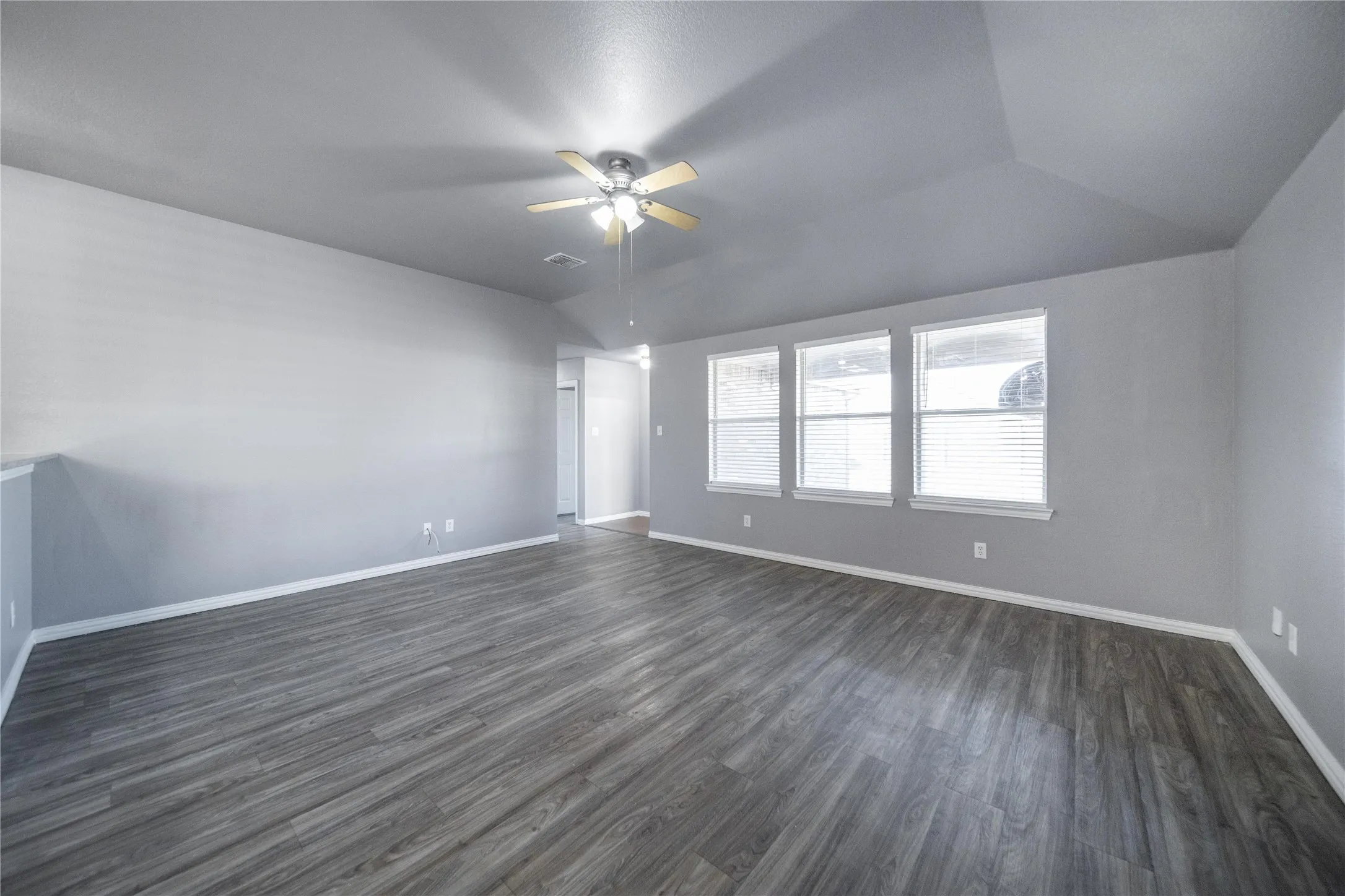 Spacious living area featuring wood-finish flooring, vaulted ceilings, and a ceiling fan