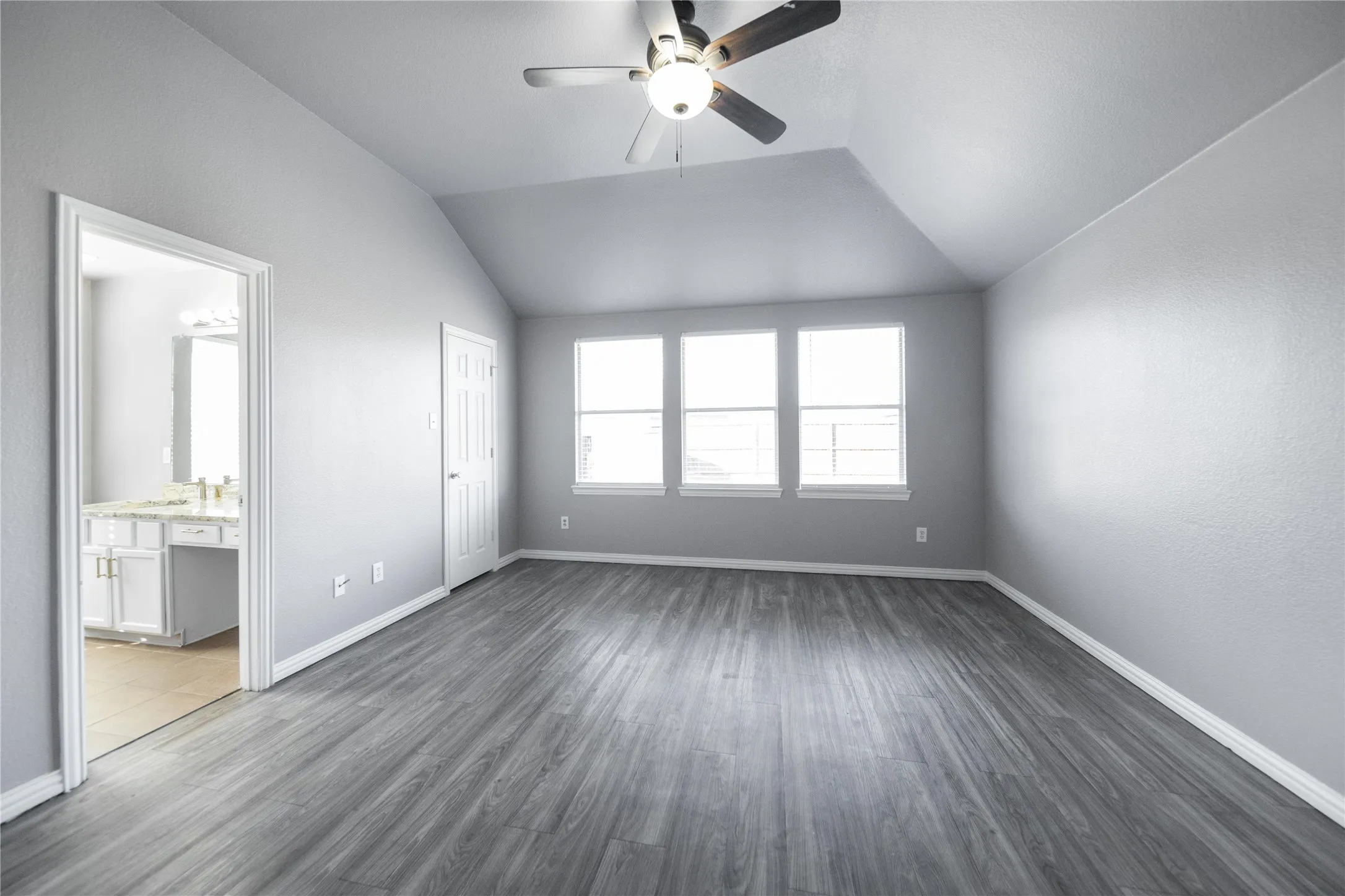 Spacious room featuring vaulted ceilings, wood-finish flooring, and a ceiling fan with integrated lighting