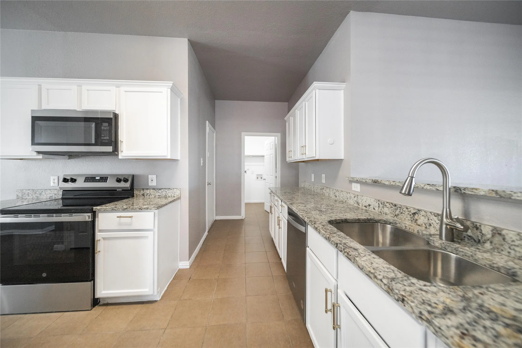 Modern kitchen featuring stainless steel appliances, white cabinetry, granite countertops, and tile flooring