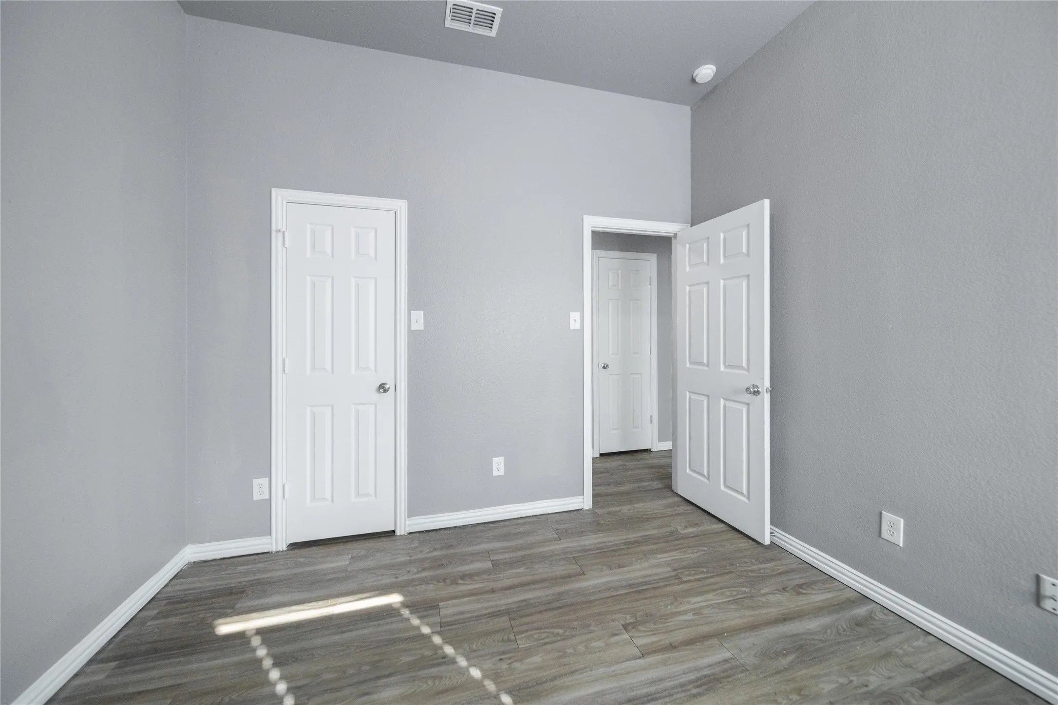 Room featuring wood-finish flooring, light grey painted walls, white baseboards, and a white six-panel door