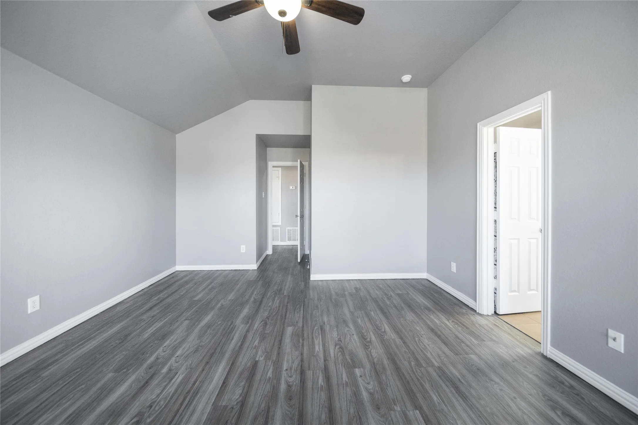 Spacious room featuring wood-finish flooring, light gray wall paint, white trim, and a ceiling fan with integrated lighting