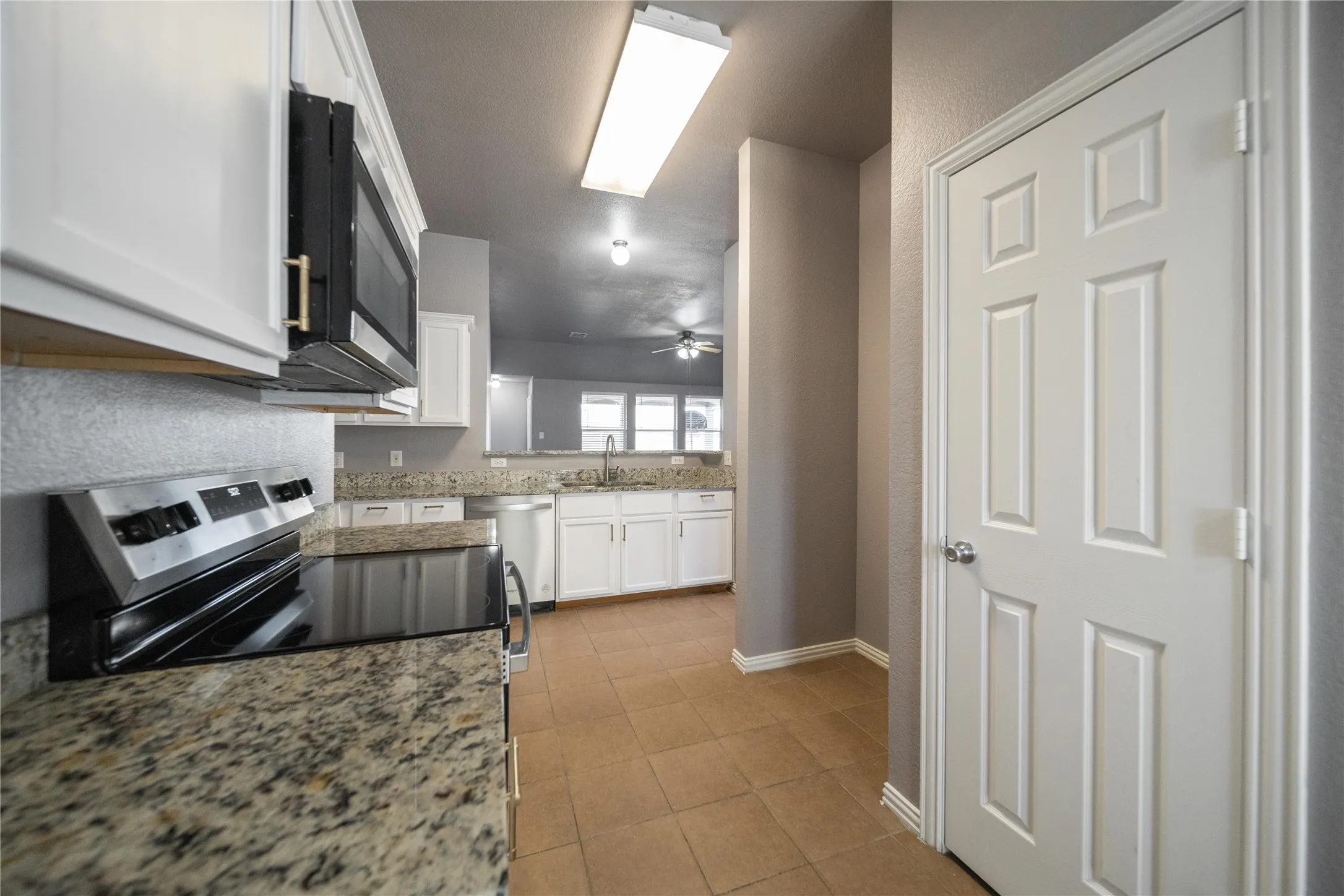 Kitchen featuring white cabinetry, speckled countertops, stainless steel appliances including a built-in microwave and range, and tile flooring