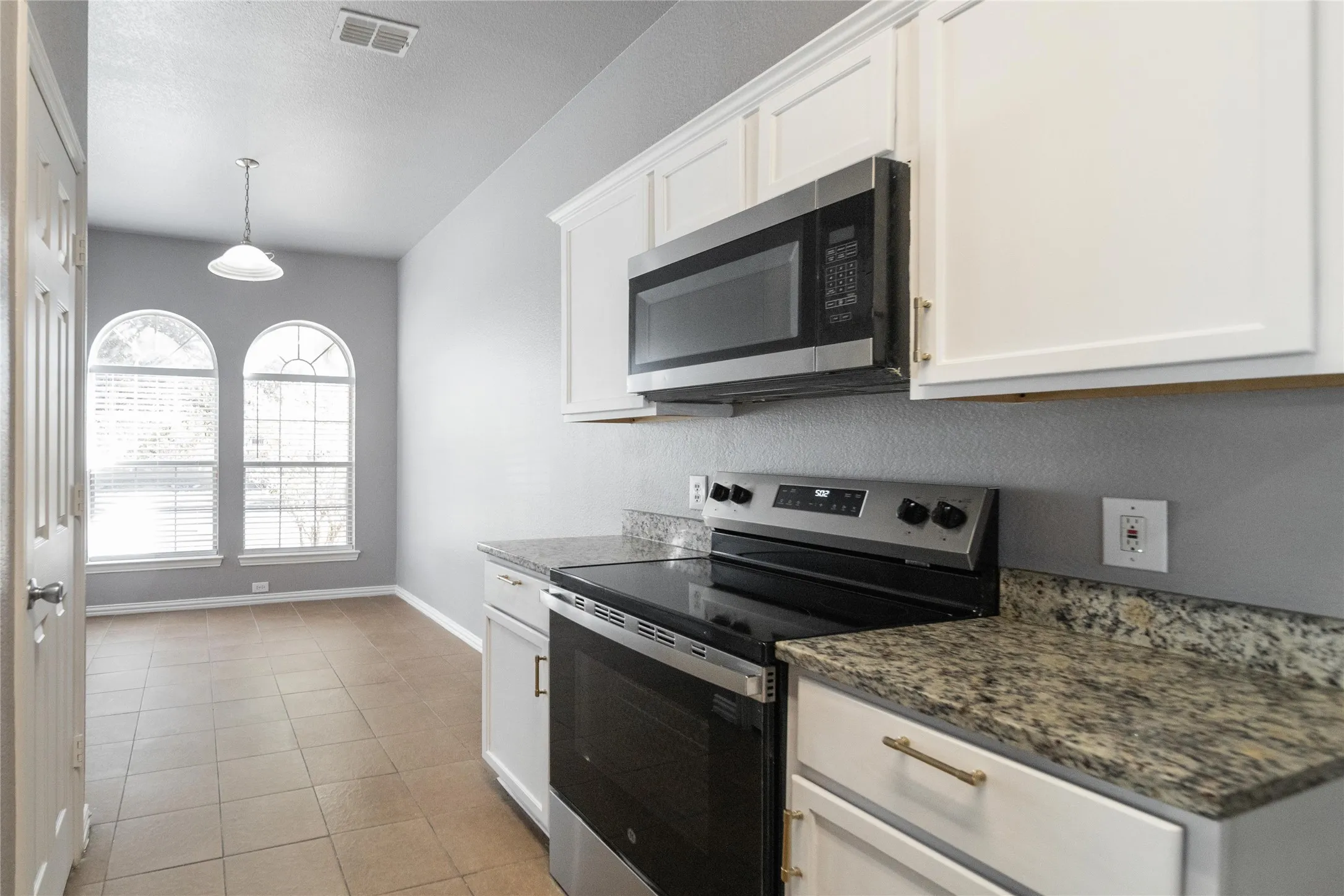Kitchen area featuring stainless steel appliances, white cabinetry with gold-tone hardware, and speckled countertops