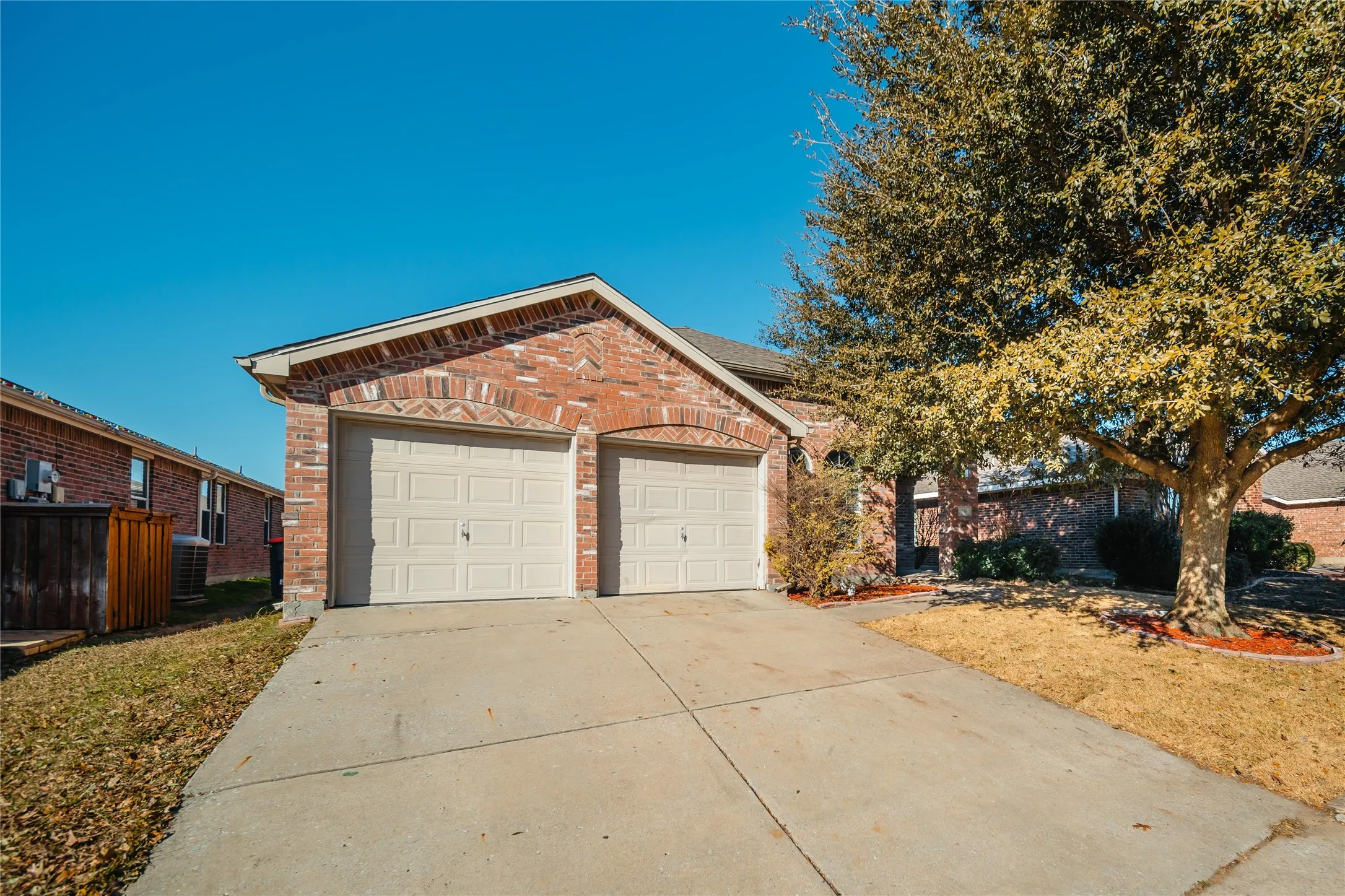 Brick facade property featuring a two-car garage with arched lintels, a concrete driveway, and mature landscaping with a prominent tree