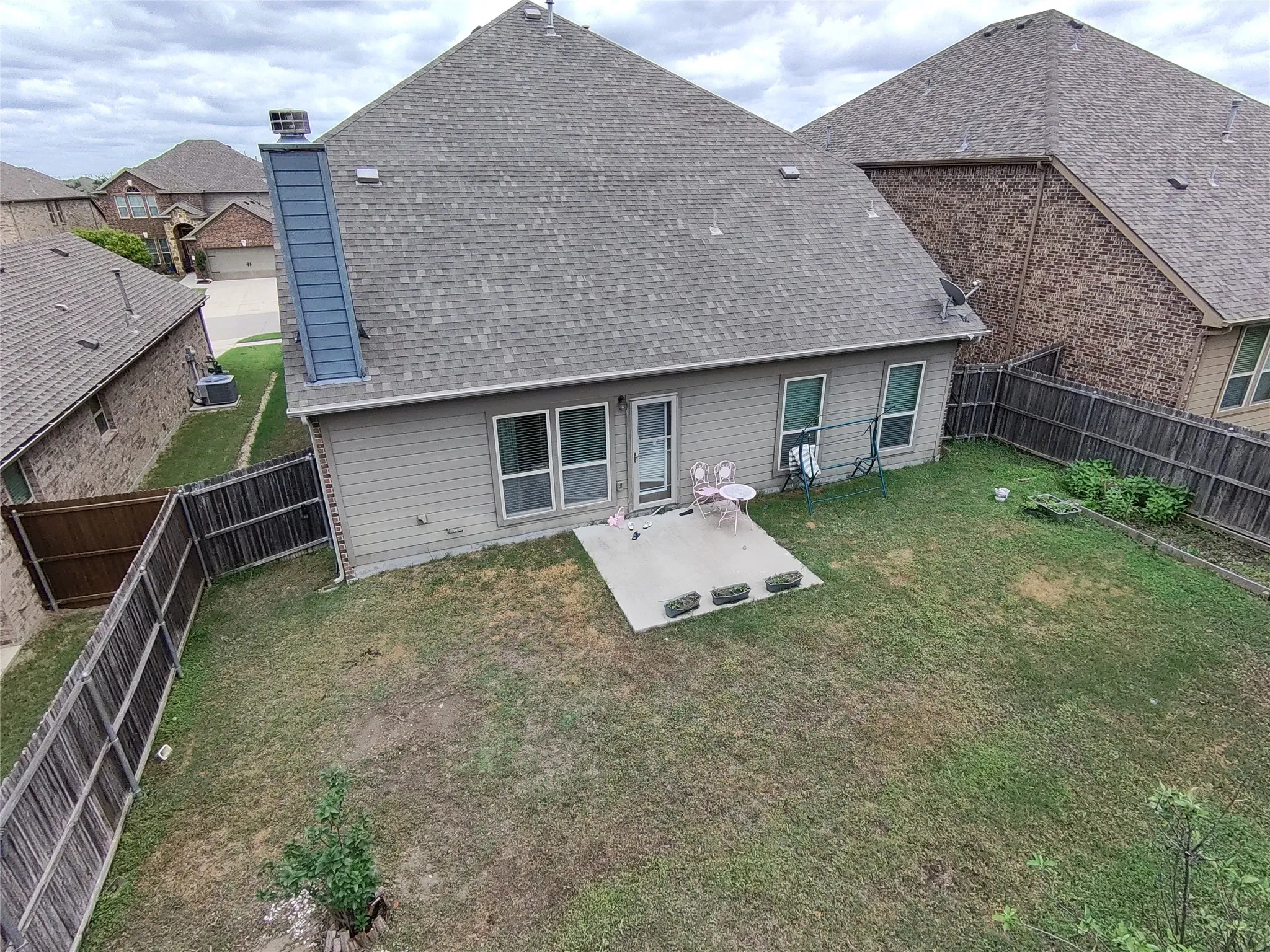 Exterior rear featuring a concrete patio, a private fenced yard, a pitched shingle roof, and a chimney with vertical siding