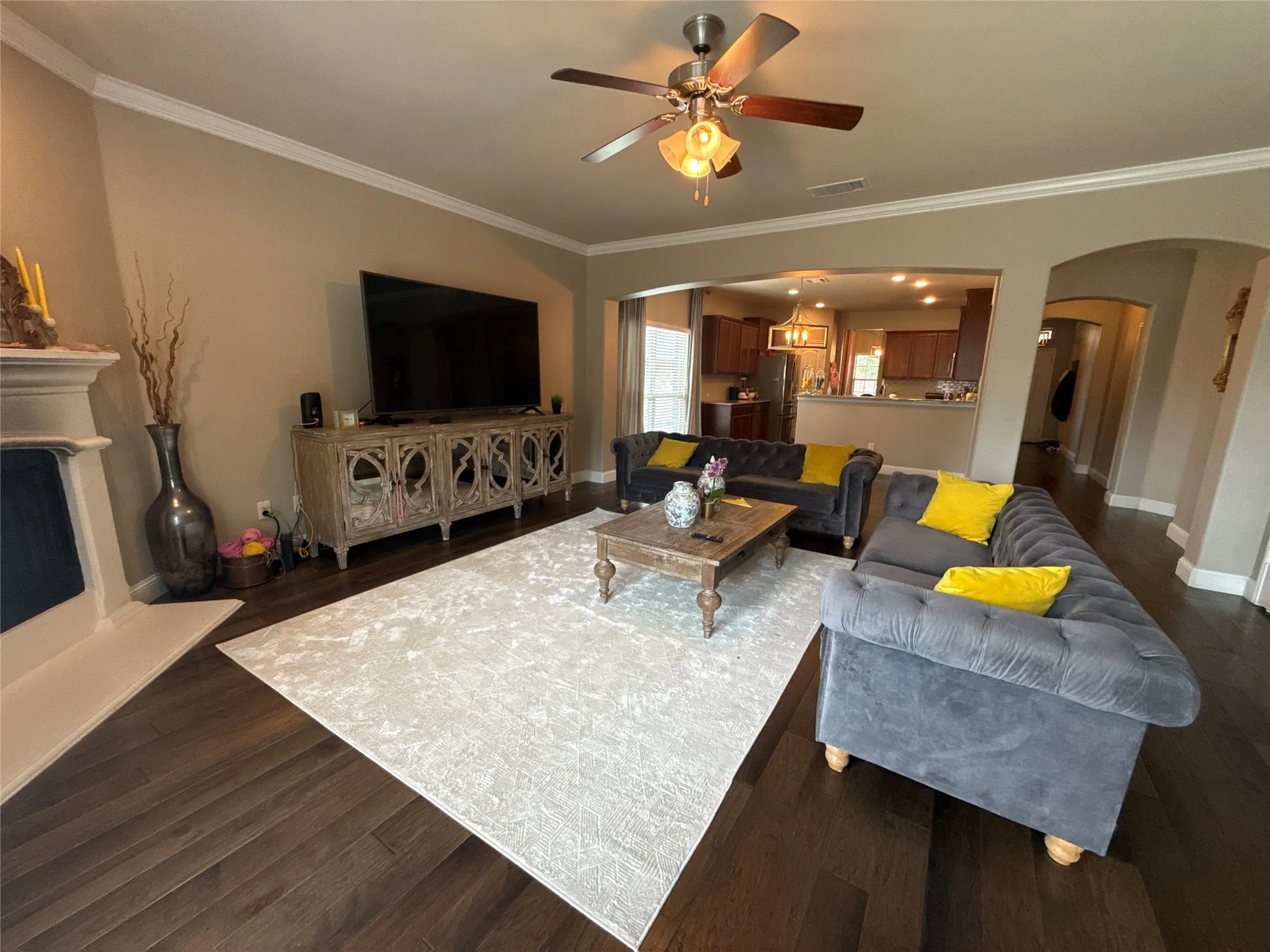 Spacious living area featuring wood-finish flooring, crown molding, and a ceiling fan with integrated lighting