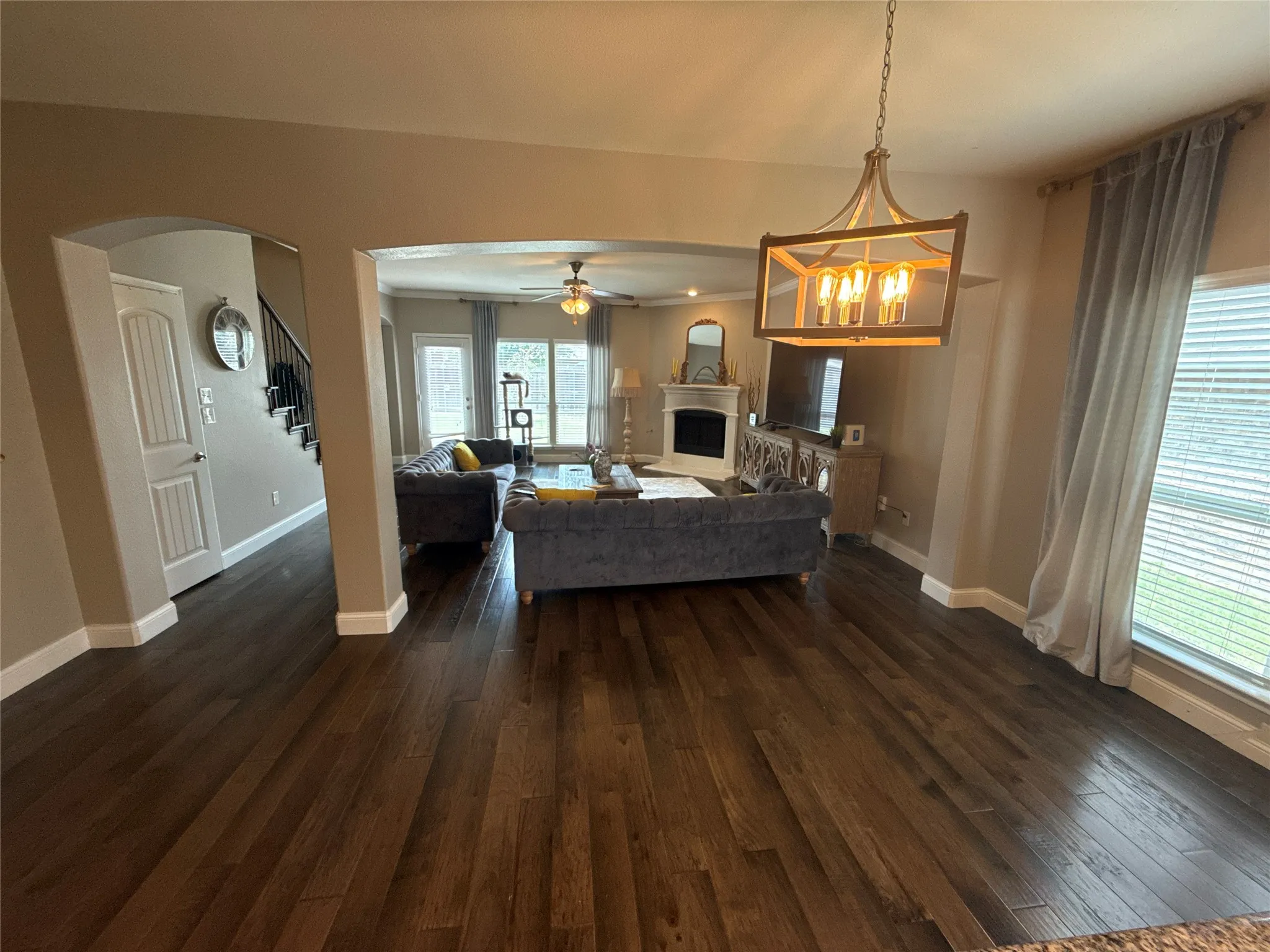 Rich wood-finish flooring throughout, featuring an arched entryway and a dining area with a linear chandelier