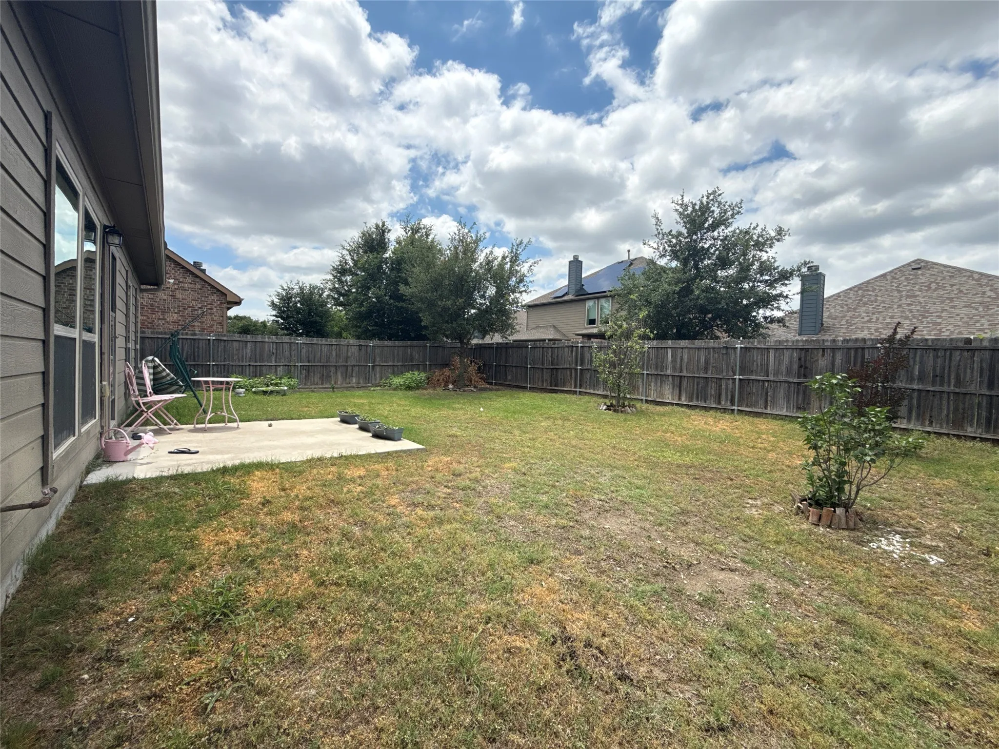 Spacious backyard featuring a concrete patio, wood privacy fencing, and mature trees