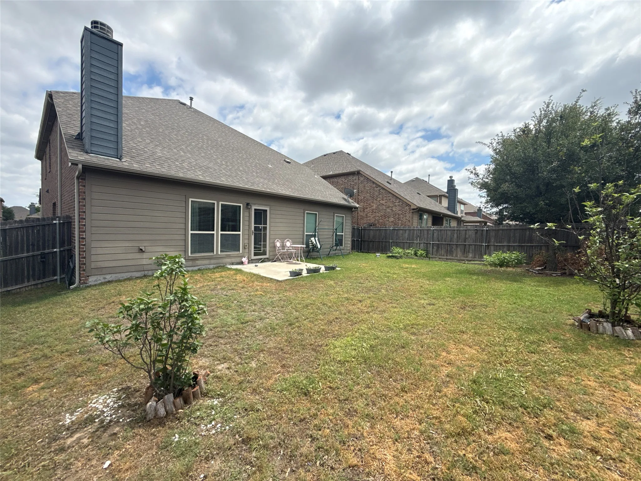 Spacious backyard featuring a concrete patio, wood fence, and mature trees