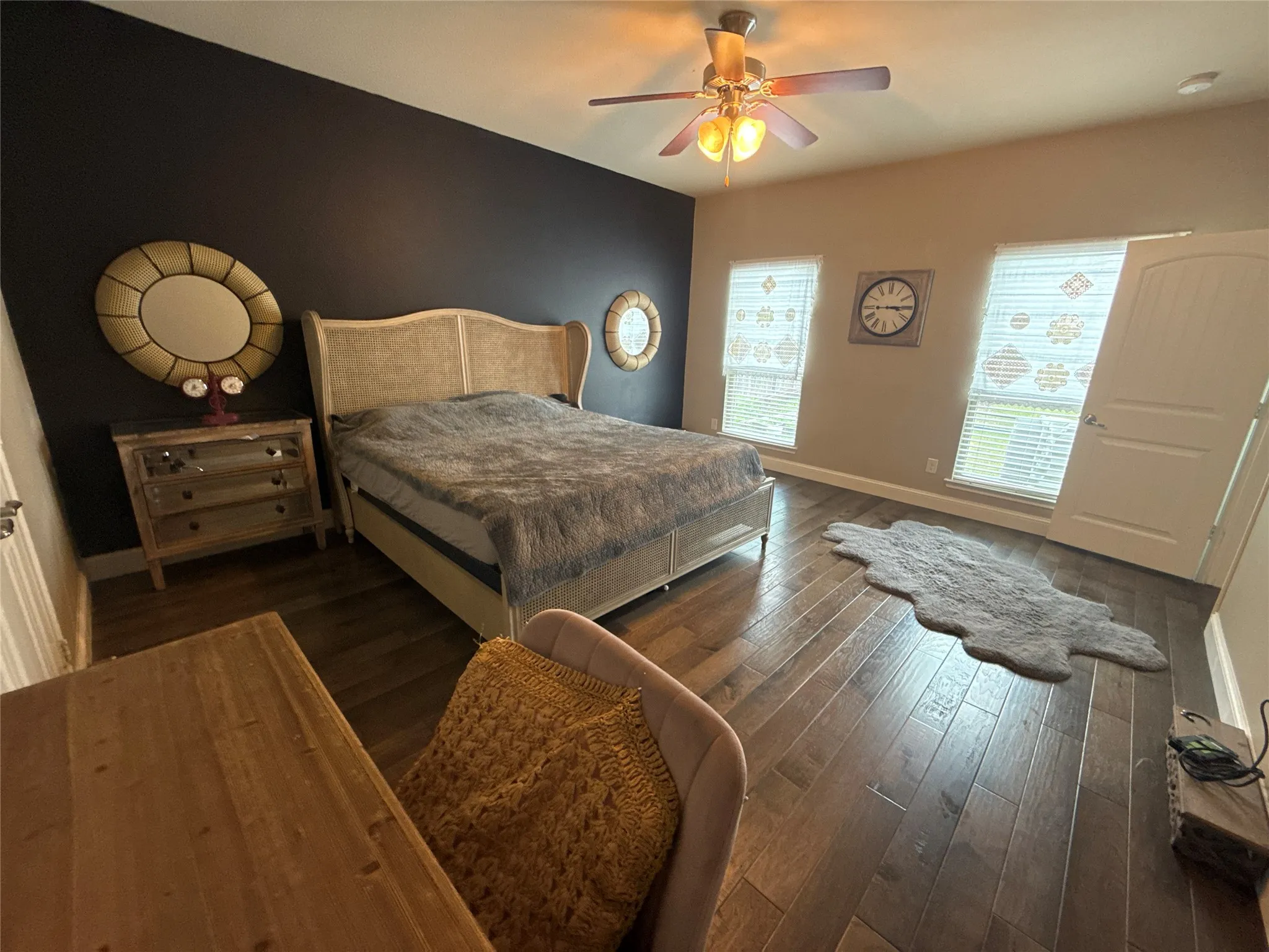 Bedroom featuring dark wood-finish flooring, a ceiling fan with light fixture, and two windows with blinds
