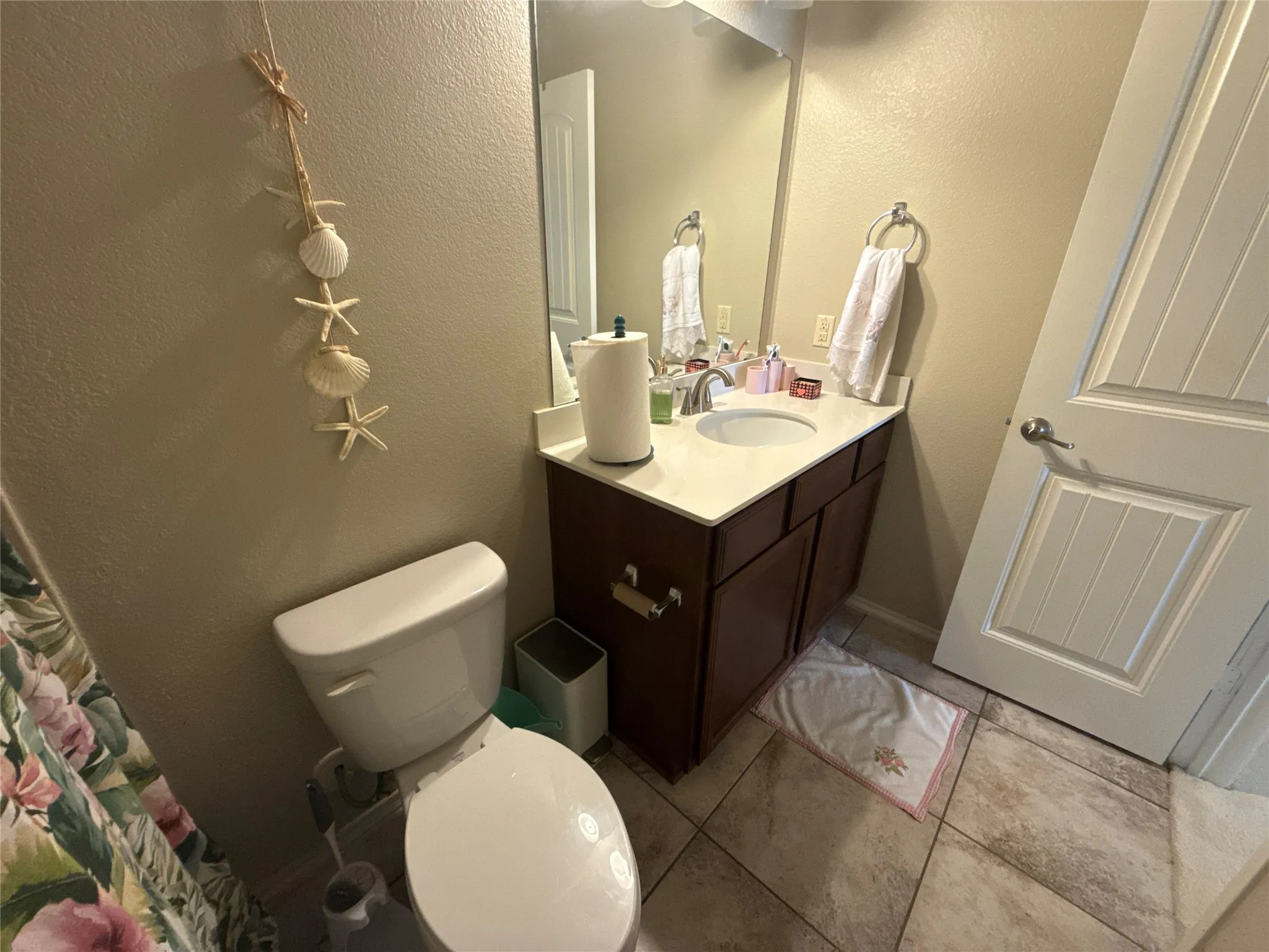 Bathroom featuring a dark wood-finish vanity with a white countertop and integrated sink, a white toilet, and neutral-toned tile flooring