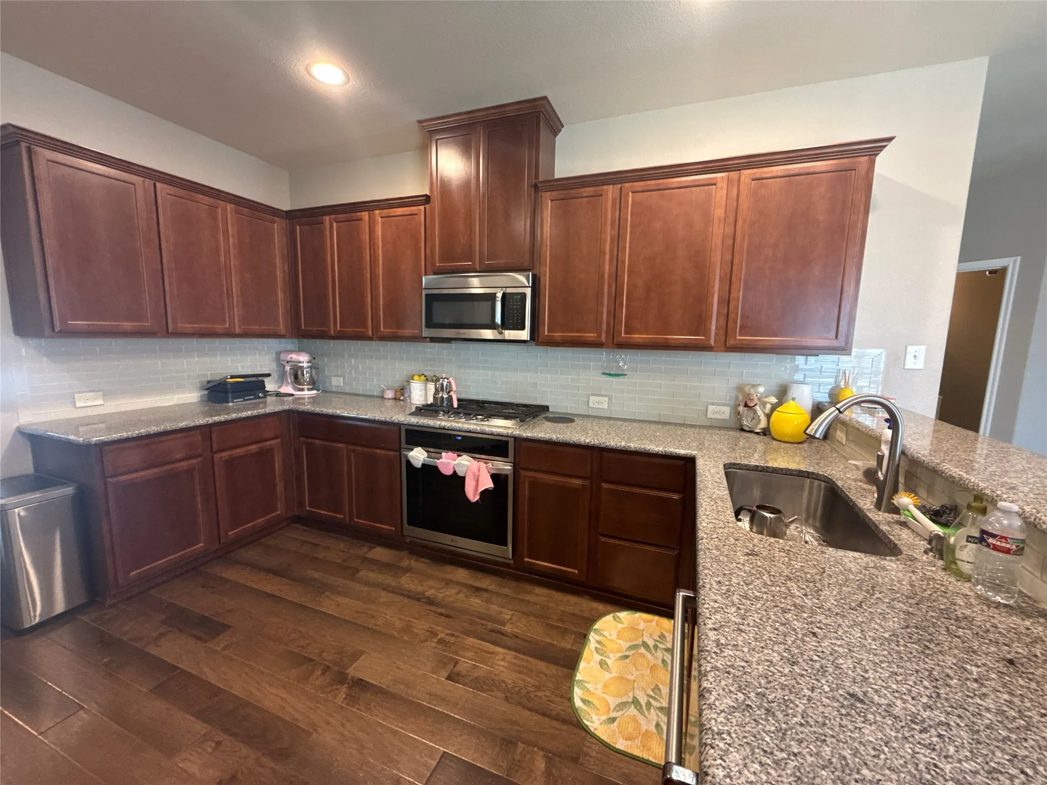 Kitchen featuring wood-finish flooring, granite countertops, tile backsplash, stainless steel appliances, and abundant cabinetry