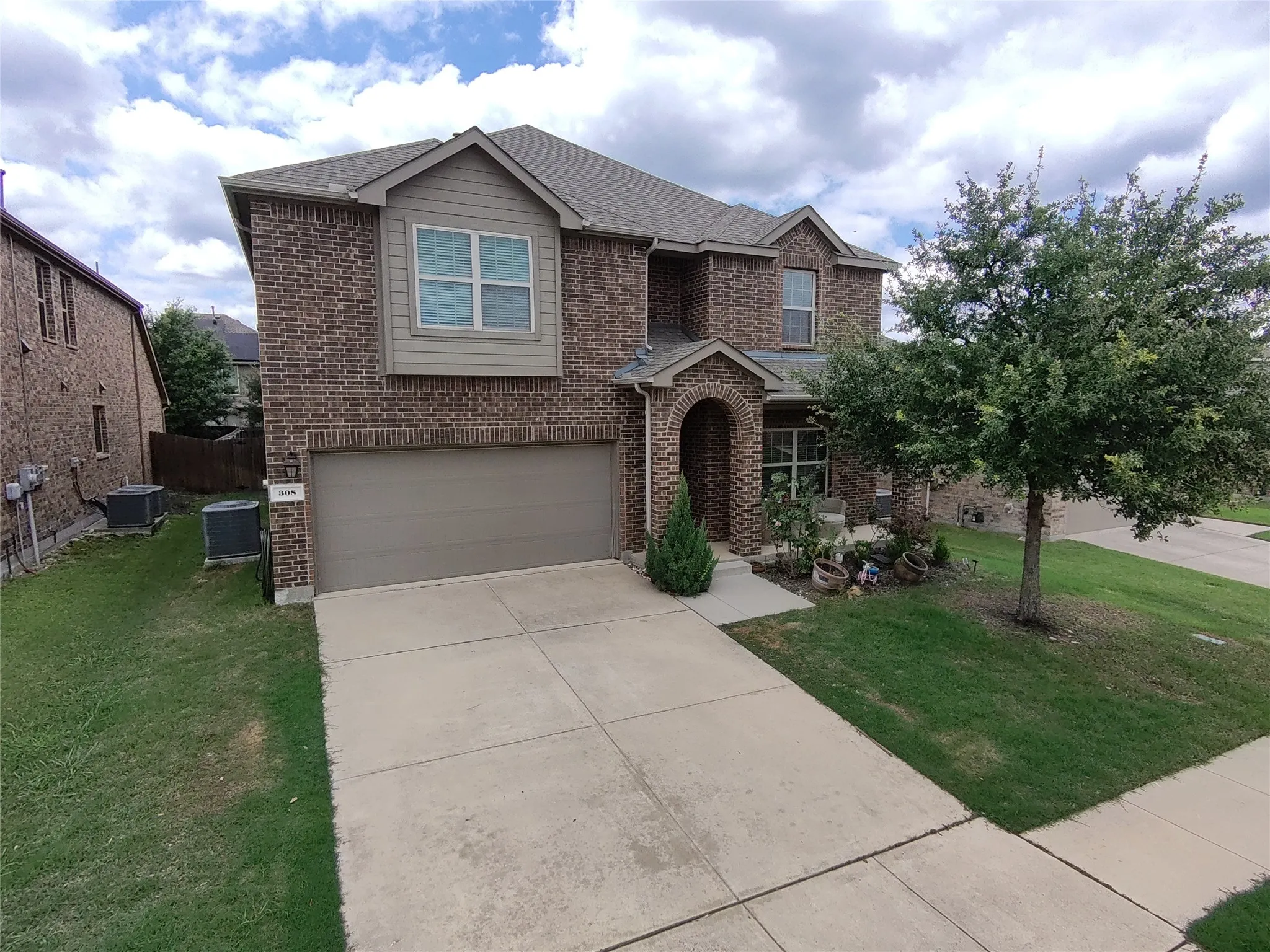 Two-story brick exterior with an arched entryway, attached garage, and landscaped front yard with mature trees