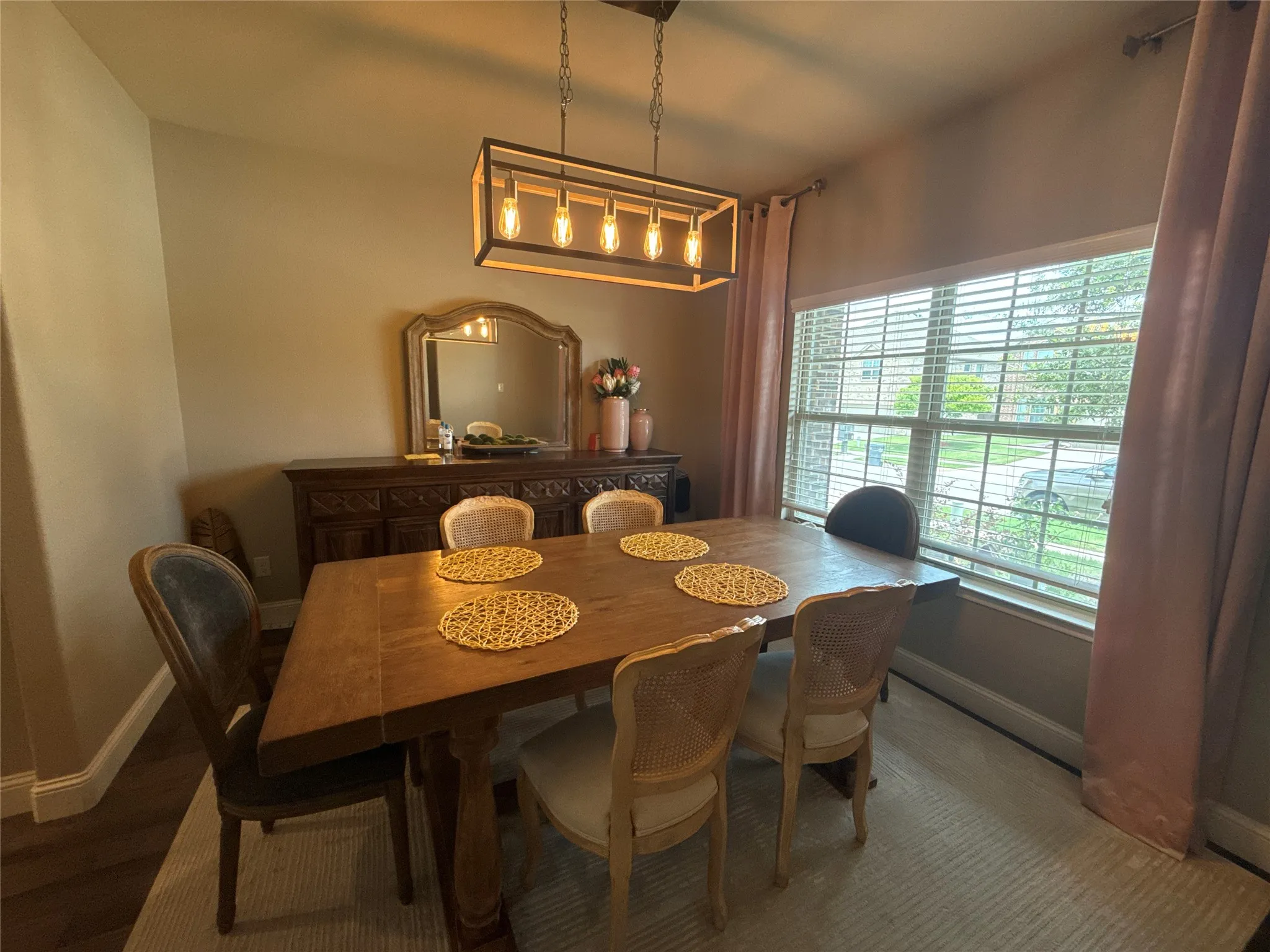 Dining area featuring a wood-finish flooring, a contemporary linear chandelier, a large window with blinds, and a built-in sideboard