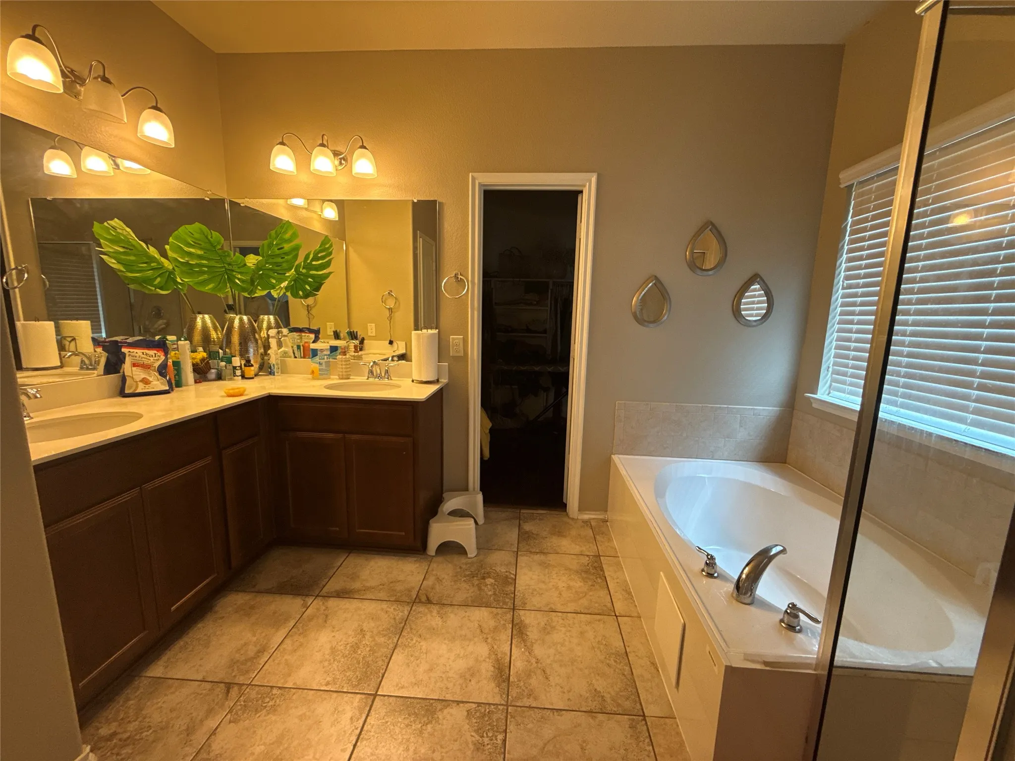 Double vanity with dual undermount sinks and extensive counter space, rich wood-finish cabinetry, ceramic tile flooring, and a built-in soaking tub with chrome fixtures
