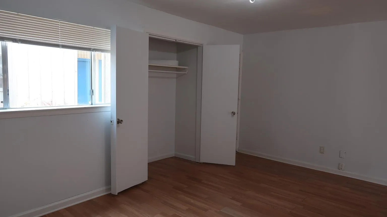 Bedroom featuring wood-finish flooring, a window with horizontal blinds, and a closet with bifold doors