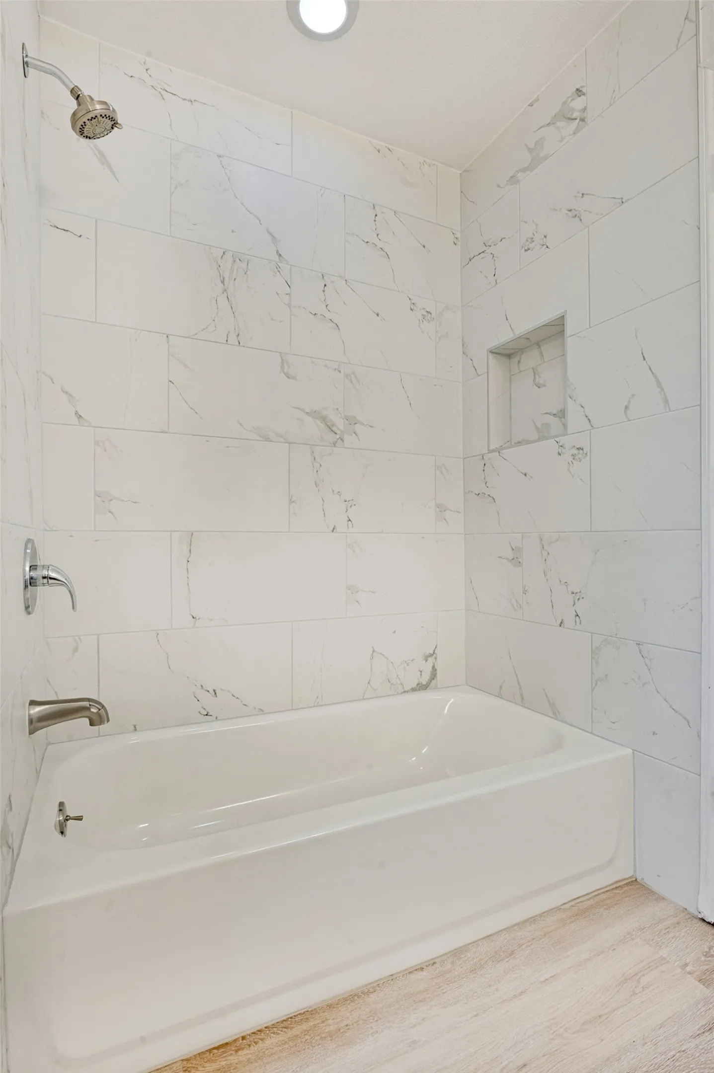 Bathtub with white subway tile surround, featuring a recessed niche and brushed nickel fixtures
