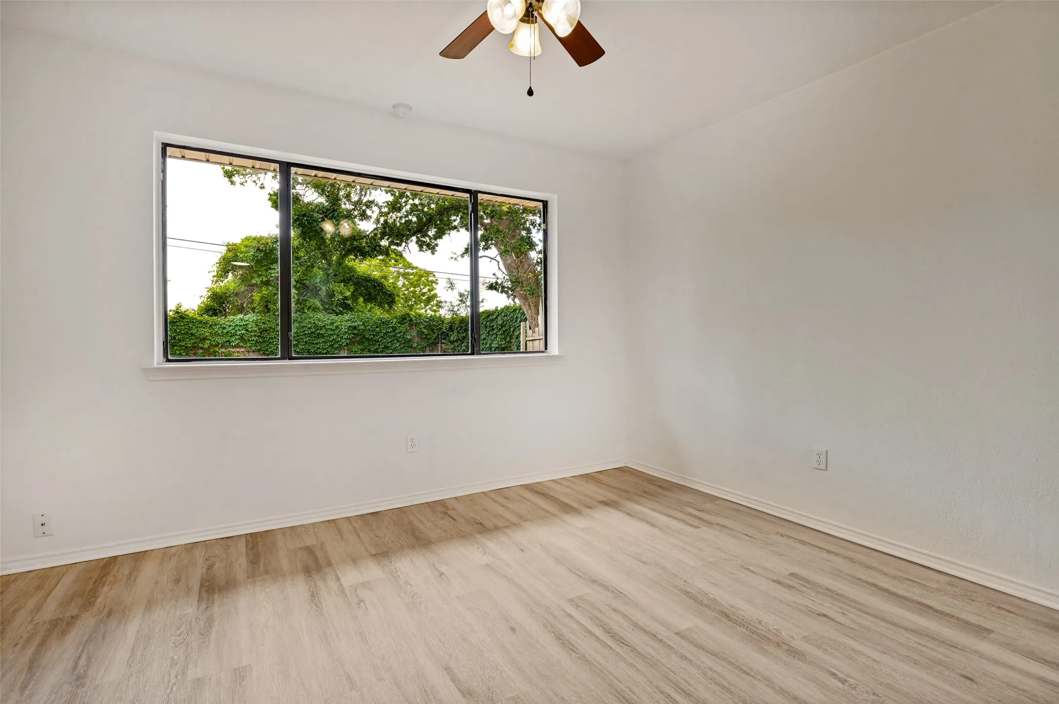 Room featuring wood-finish flooring, a large multi-pane window with a white sill, a ceiling fan with integrated lighting, and neutral wall paint