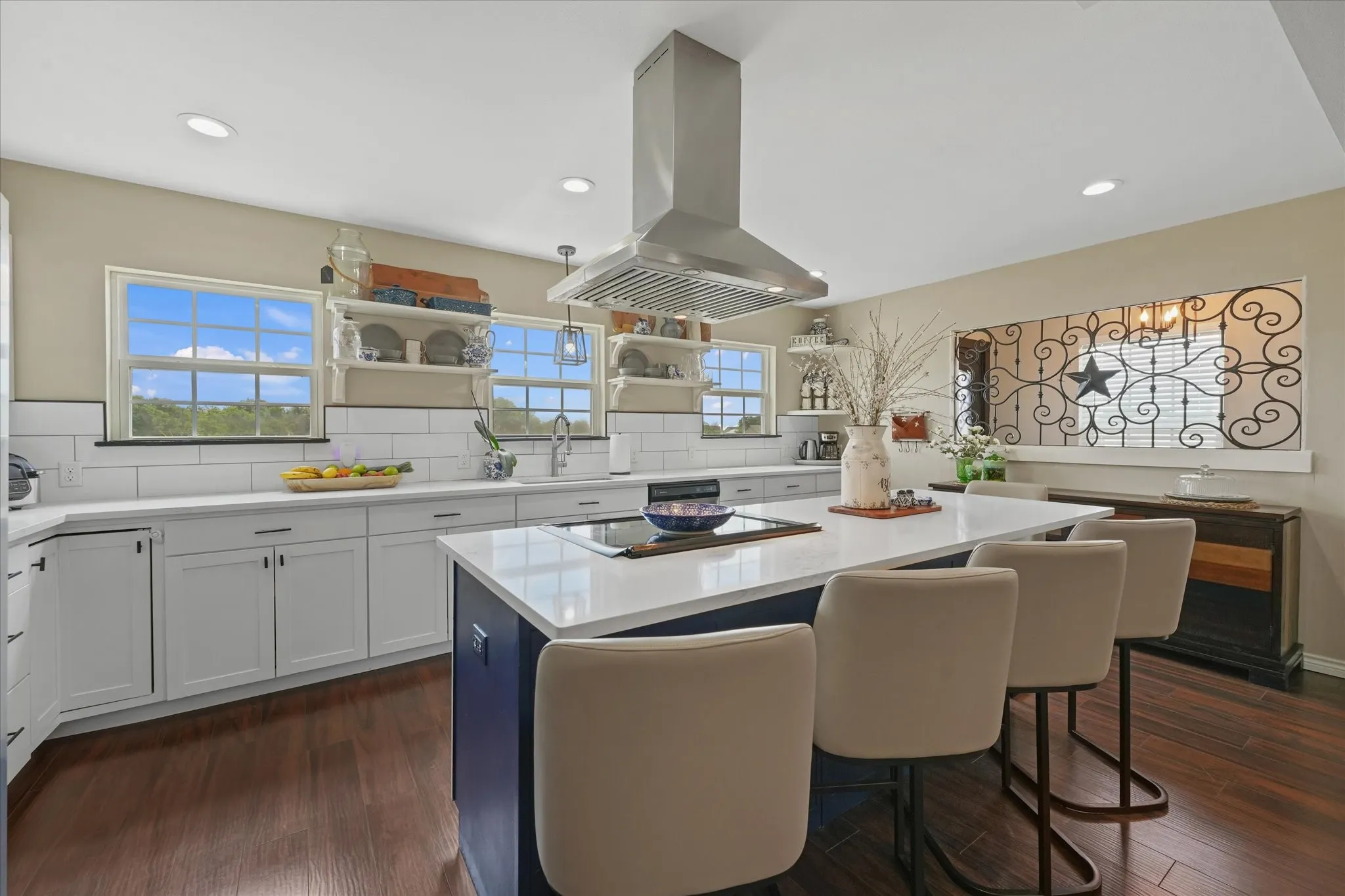 Kitchen featuring an expansive center island with seating, white shaker cabinetry, an undermount sink, a stainless steel range hood, and wood-finish flooring