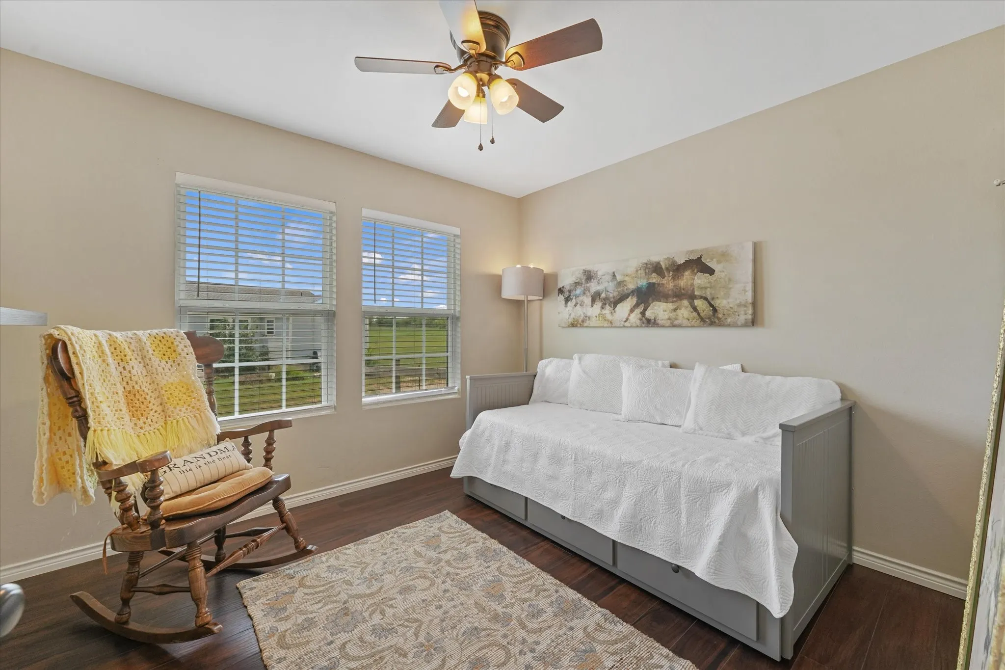 Bright room featuring two windows with horizontal blinds, dark wood-finish flooring, a ceiling fan with integrated lighting, and neutral wall paint
