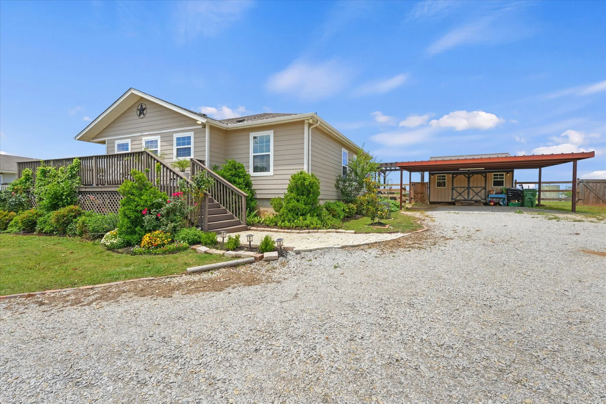 Exterior featuring an expansive gravel driveway, a large raised wooden deck with stairs, mature landscaping, a detached shed, and an extended metal carport