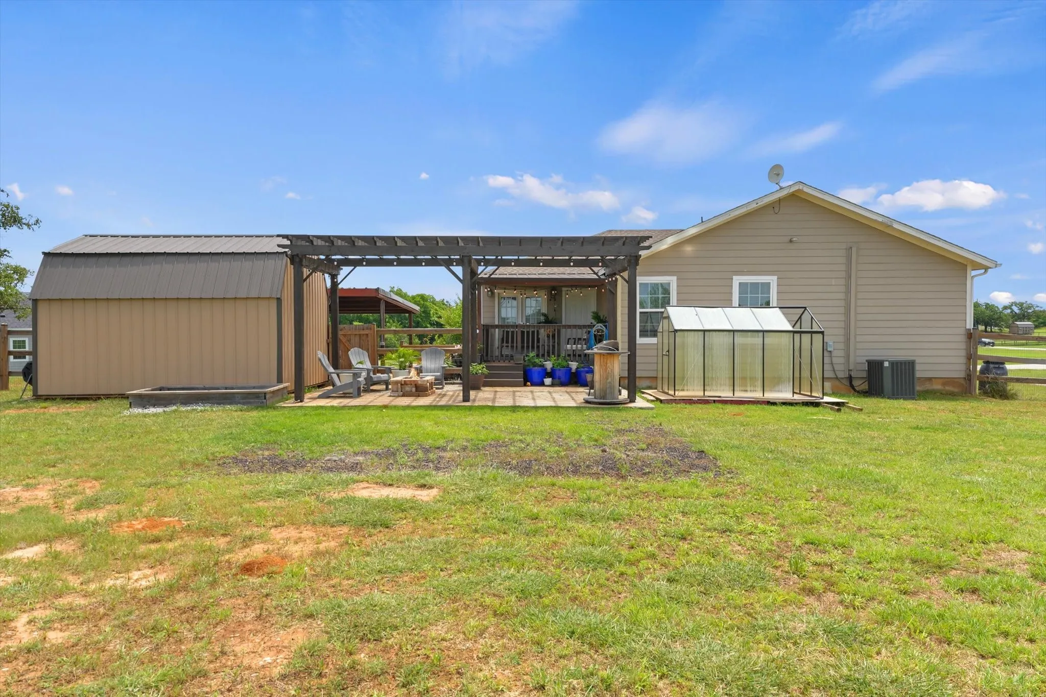 Expansive backyard featuring a pergola-covered patio, detached shed with metal roofing, and a built-in greenhouse