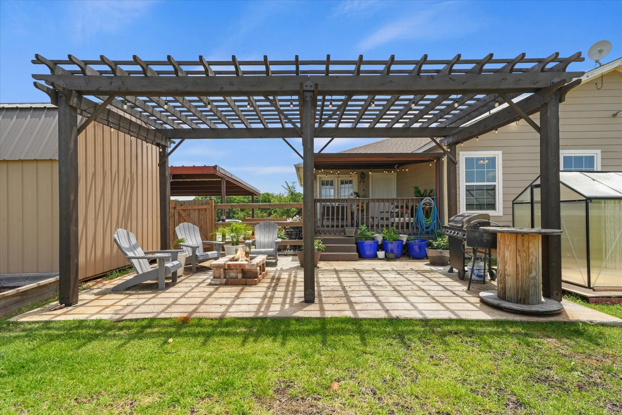 Expansive outdoor patio featuring a large wooden pergola, a built-in fire pit with brick surround, and a dedicated grilling area