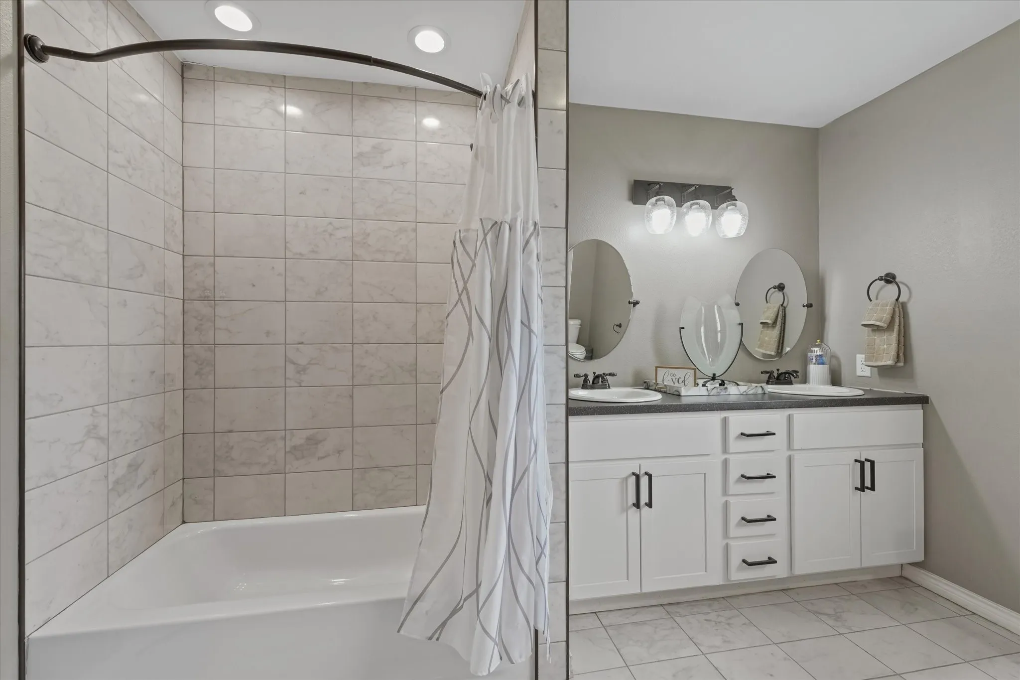Bathroom featuring a dual vanity with white cabinetry, dark countertops, and black hardware