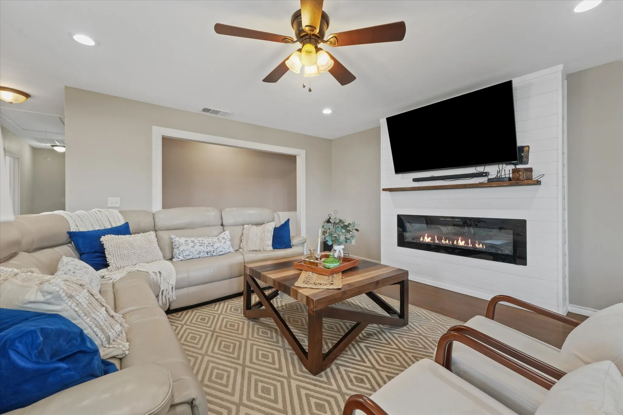 Living area featuring a shiplap accent wall with a linear fireplace, wood-finish flooring, recessed lighting, and a ceiling fan