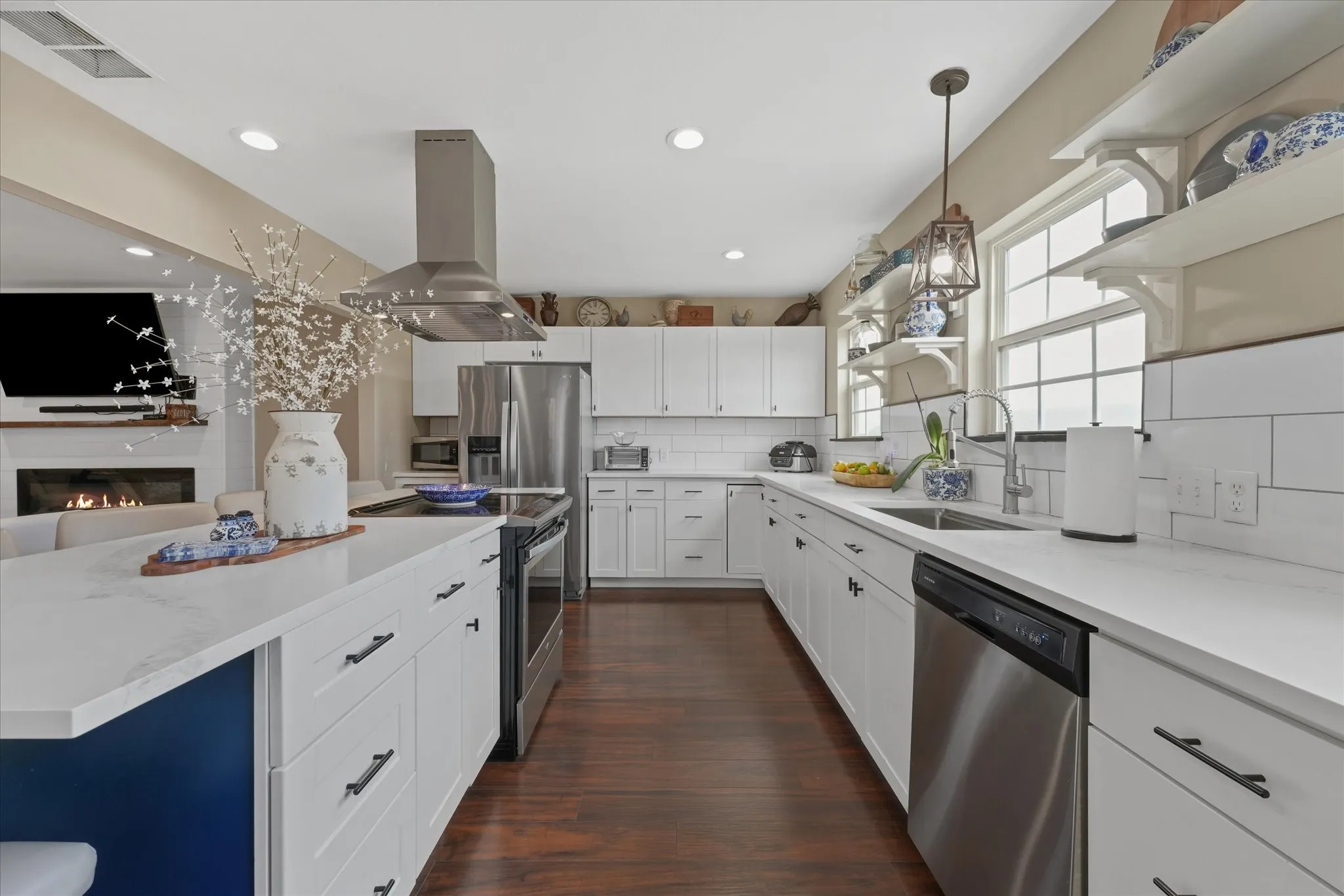 Kitchen featuring an expansive island with a white countertop and blue base, stainless steel appliances, white cabinetry, recessed lighting, and wood-finish flooring