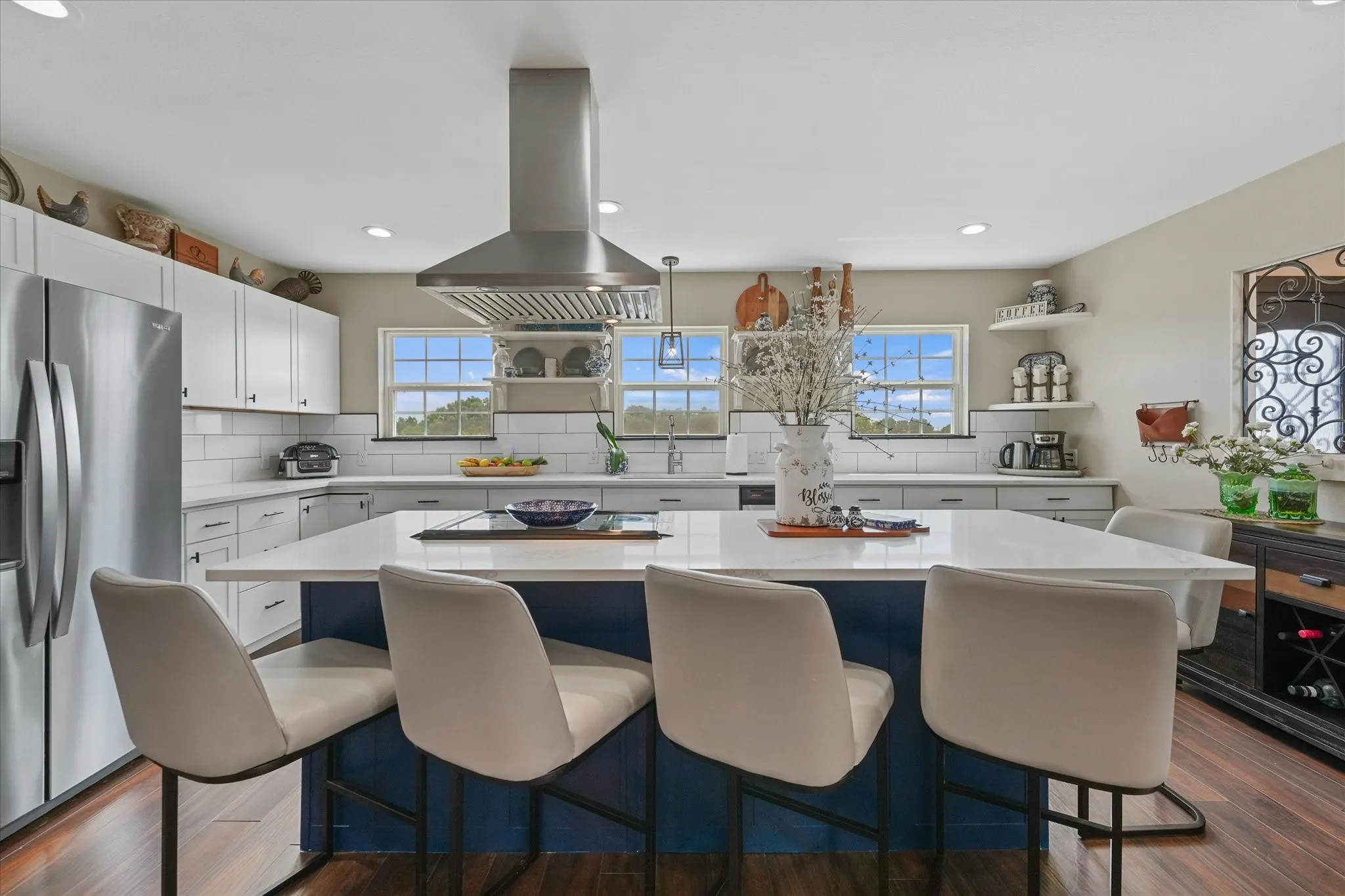 Spacious kitchen featuring a large central island with seating, stainless steel appliances, white subway tile backsplash, and wood-finish flooring