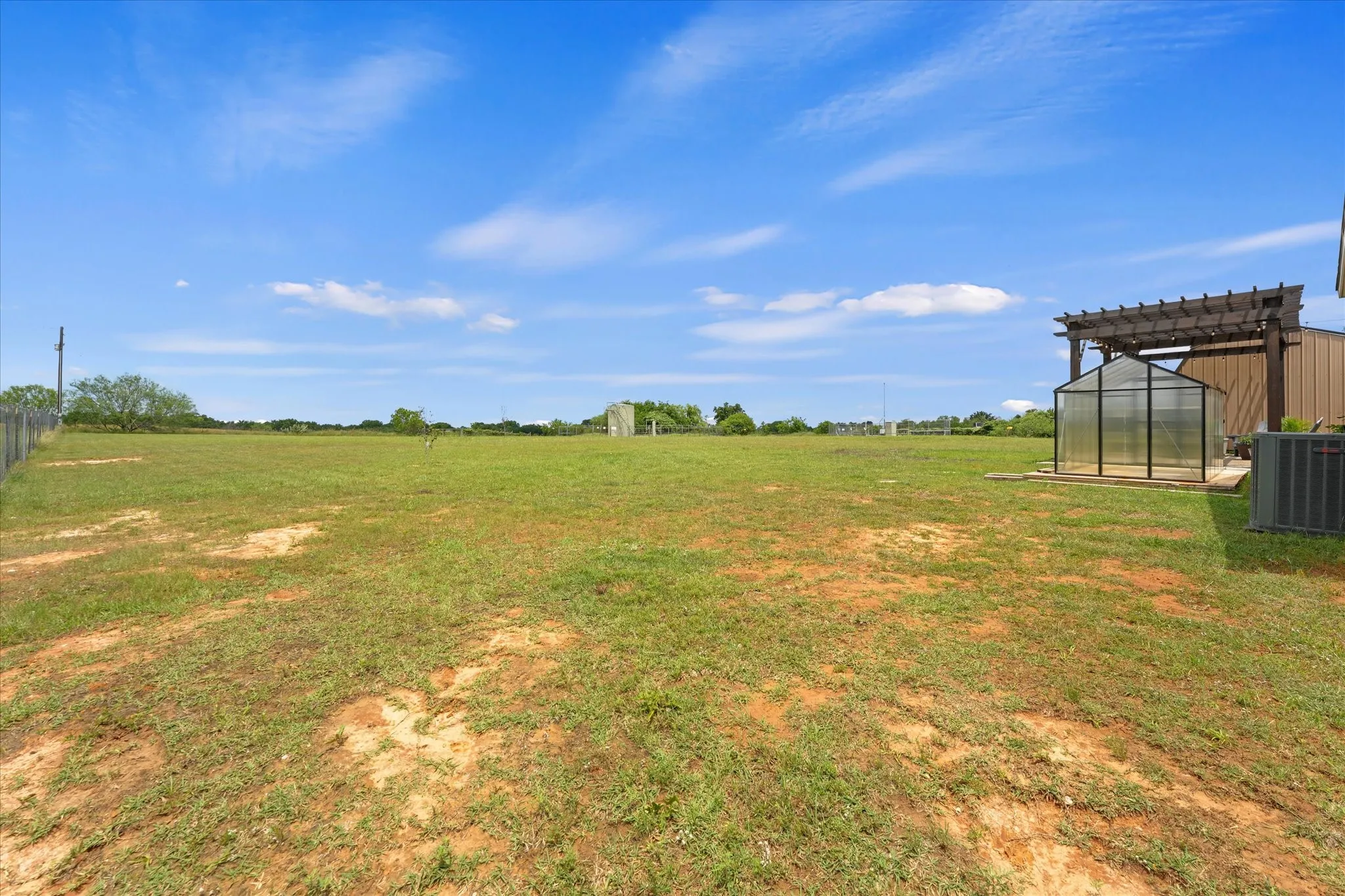 Expansive outdoor space featuring a large grassy area, a detached greenhouse, a wood pergola structure, and a perimeter fence