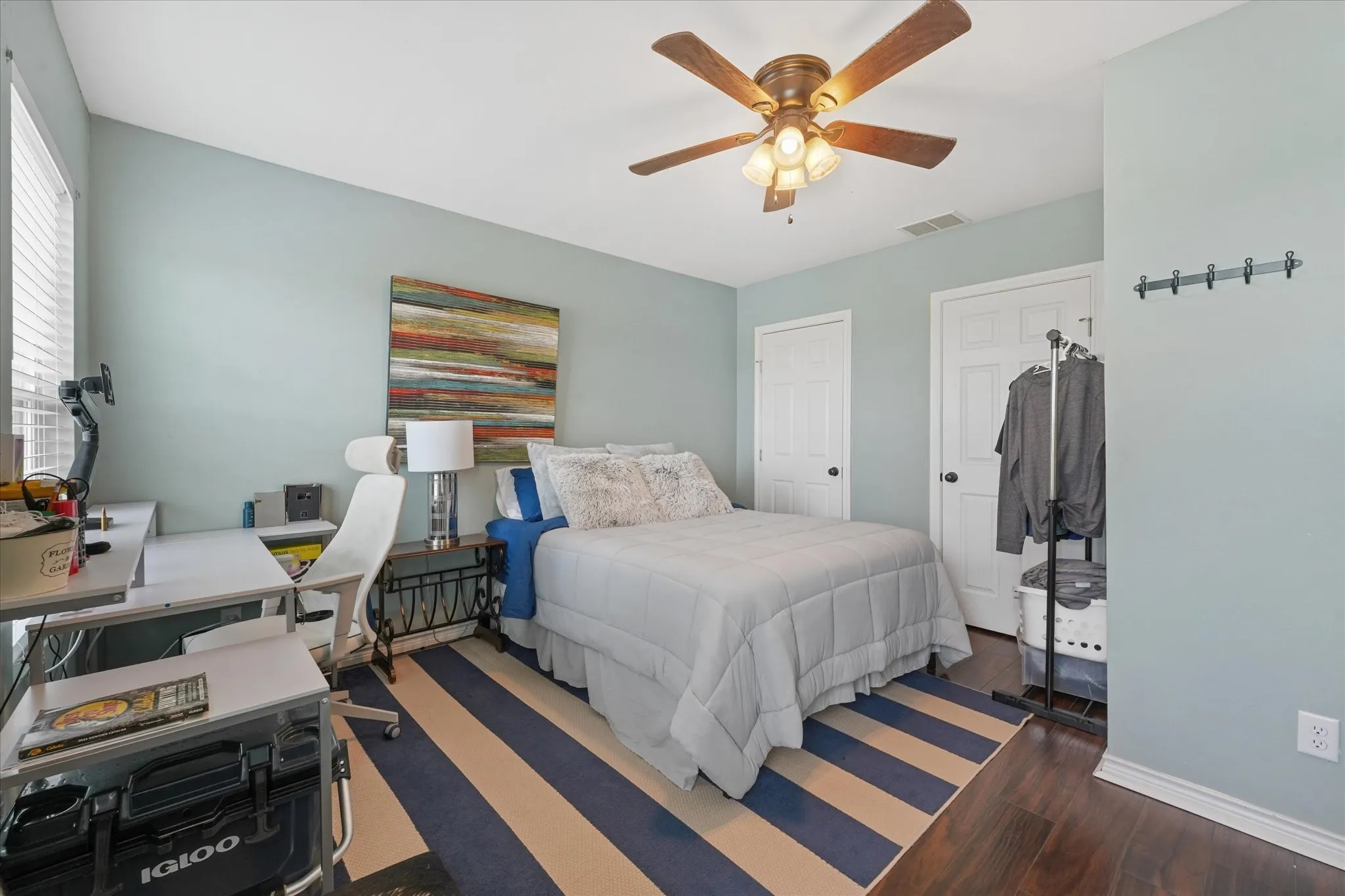 Bedroom featuring wood-finish flooring, two panel doors, a ceiling fan with integrated lighting, and a window with blinds
