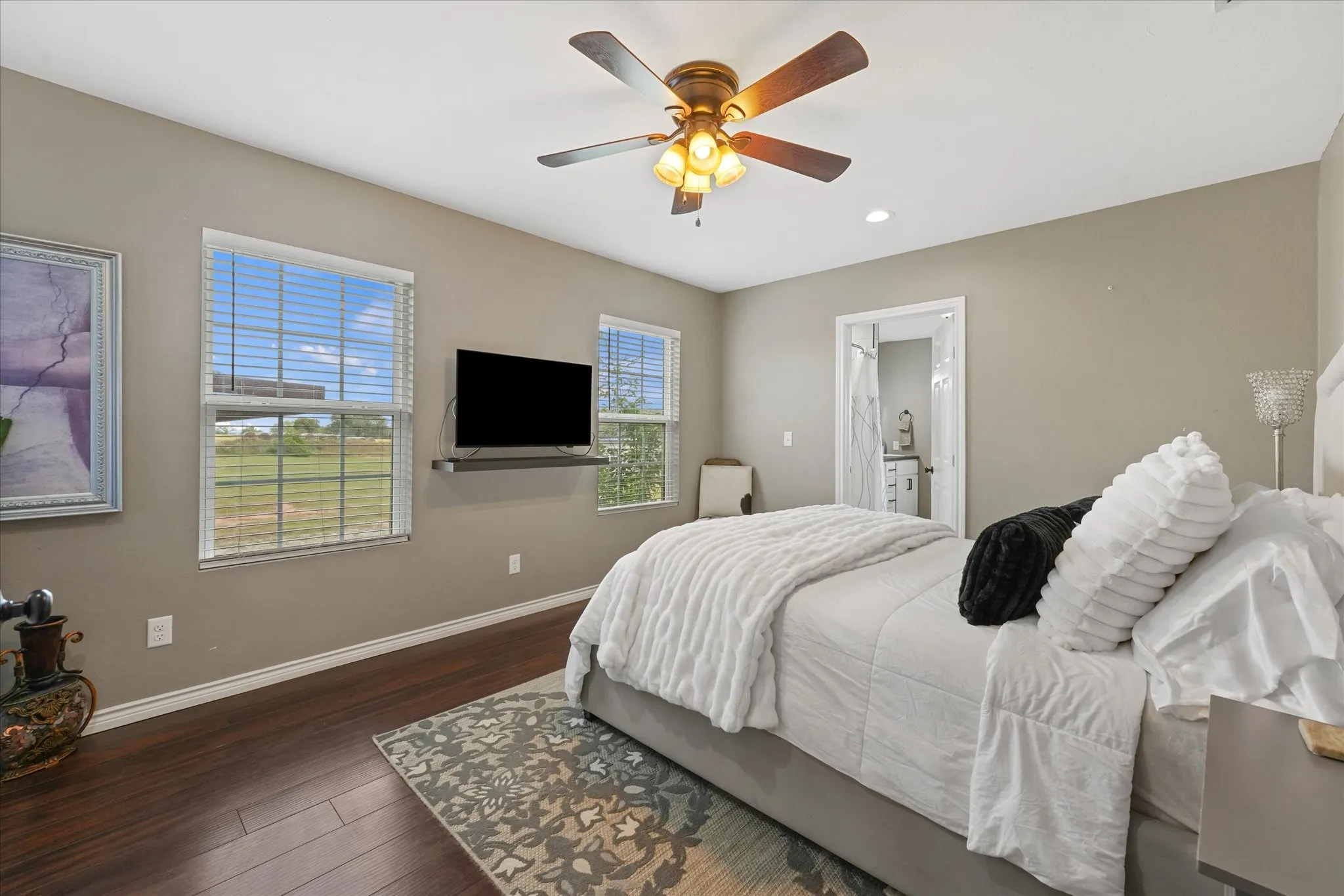 Spacious room featuring wood-finish flooring, two windows with blinds, and a ceiling fan with integrated lighting