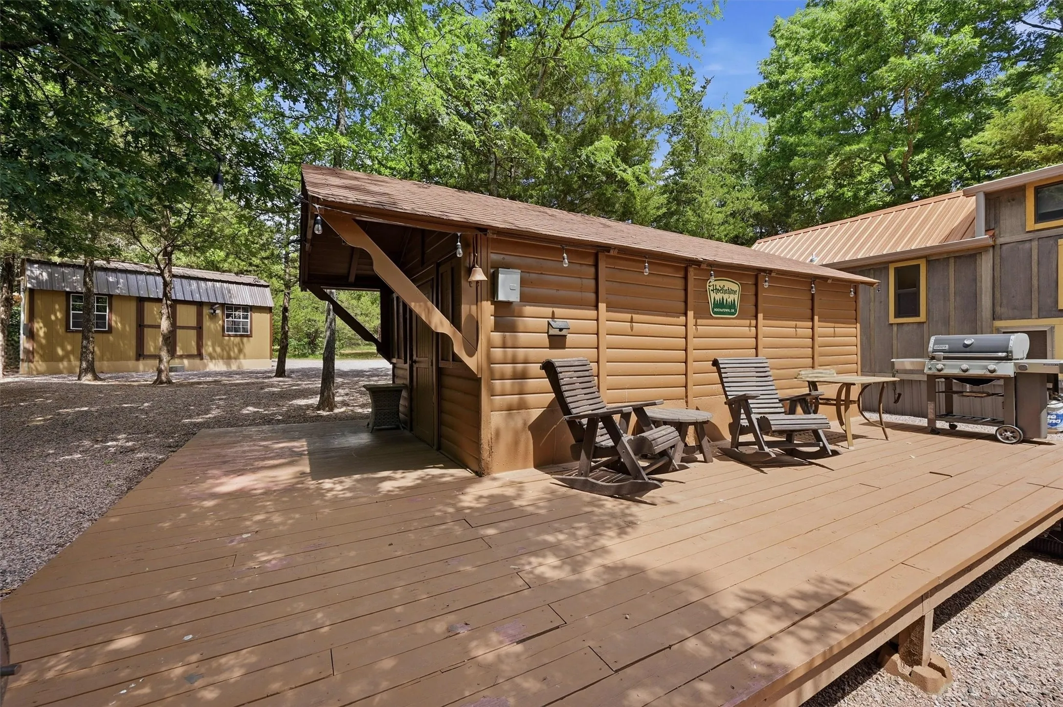 Wood-finish deck with a detached wood-sided structure featuring an extended overhang, shingle roof, and exterior lighting