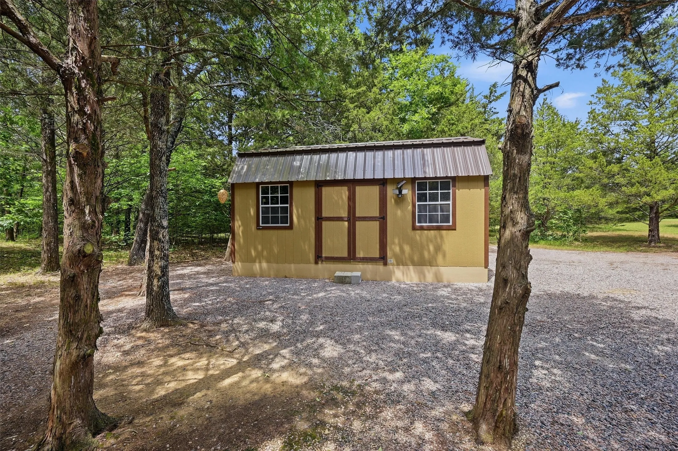 Freestanding storage structure featuring a metal roof, two windows with white trim, and a wall-mounted exterior light fixture