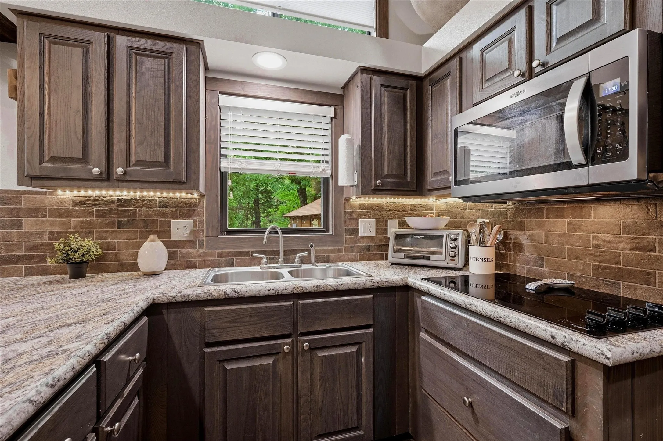 Kitchen featuring dark wood-finish cabinetry, light-toned countertops, and a brick-patterned backsplash