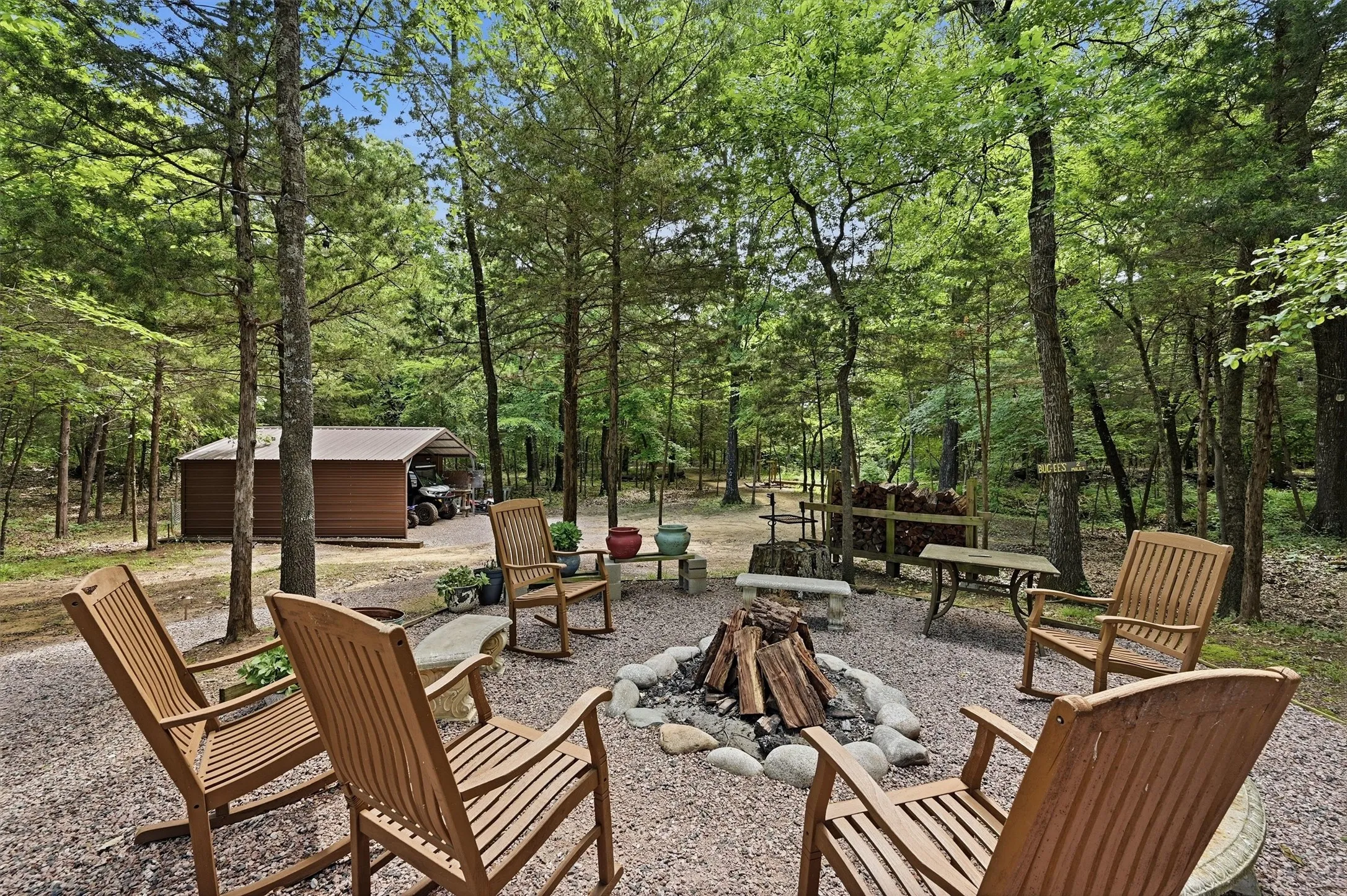 Outdoor fire pit area with stone surround, surrounded by mature trees