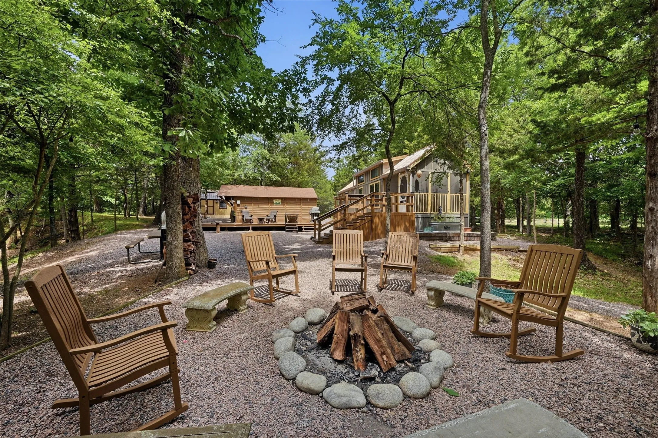 Gravel fire pit area featuring a stone border and stacked firewood
