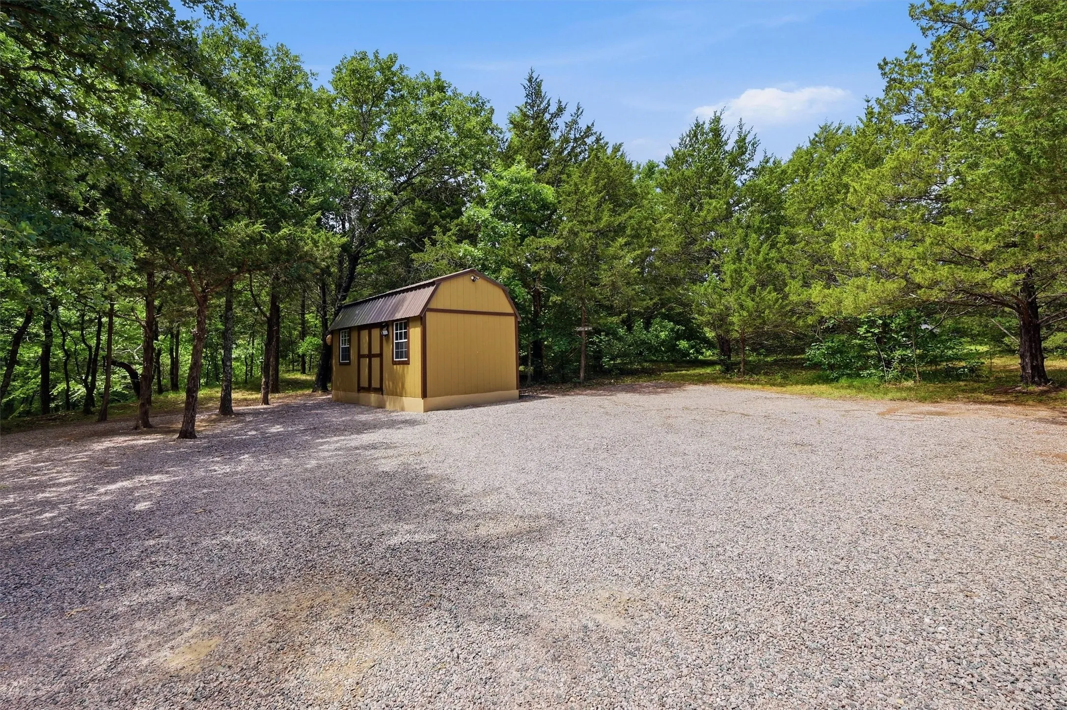 Gravel lot featuring a detached storage shed with a gambrel roof and two windows