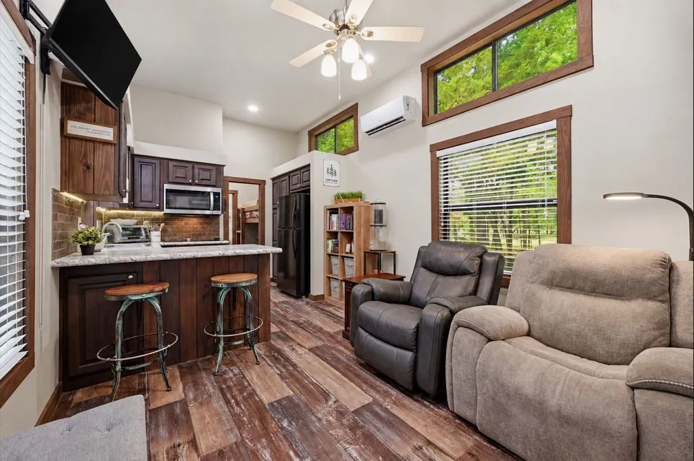 Wood-finish flooring, dark wood cabinetry, white countertops, stainless steel microwave, and a ceiling fan with integrated lighting