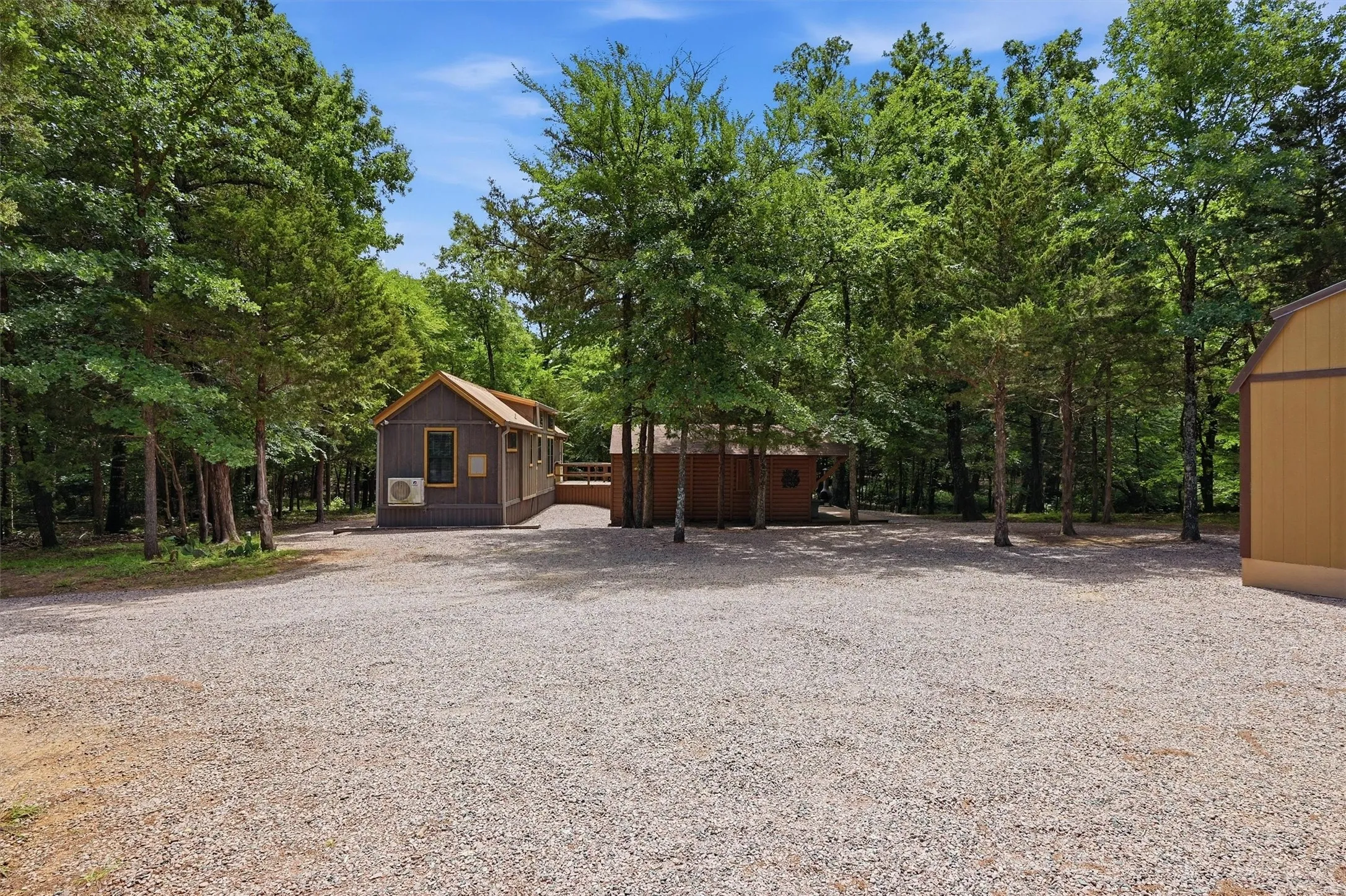 Gravel driveway with multiple structures surrounded by mature trees