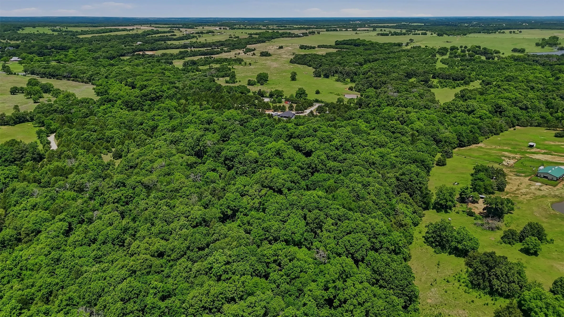 Expansive tree-covered acreage with a visible property structure nestled within the dense foliage