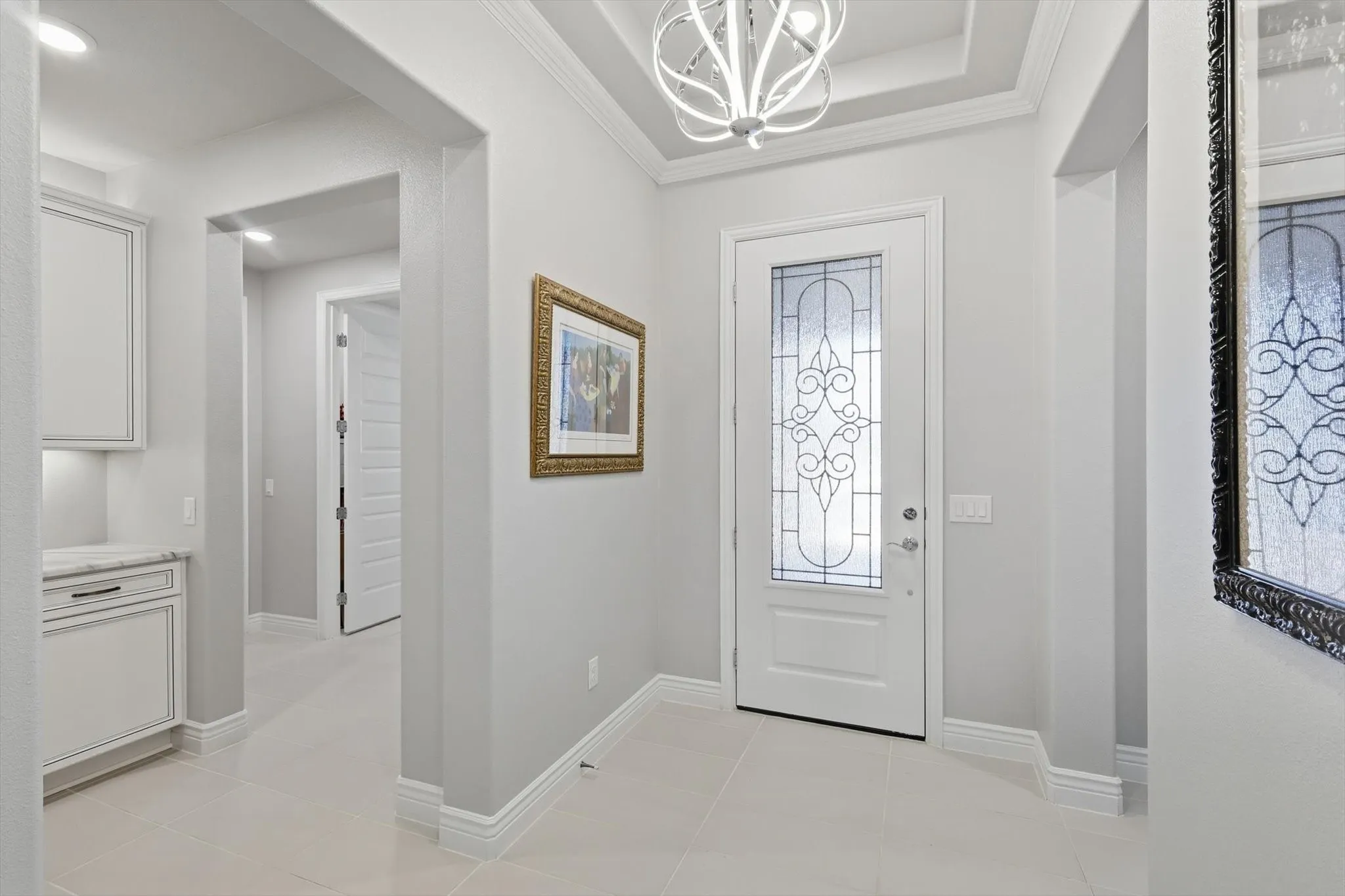 Elegant entry featuring a decorative glass front door, tray ceiling with a contemporary chandelier, and large format tile flooring